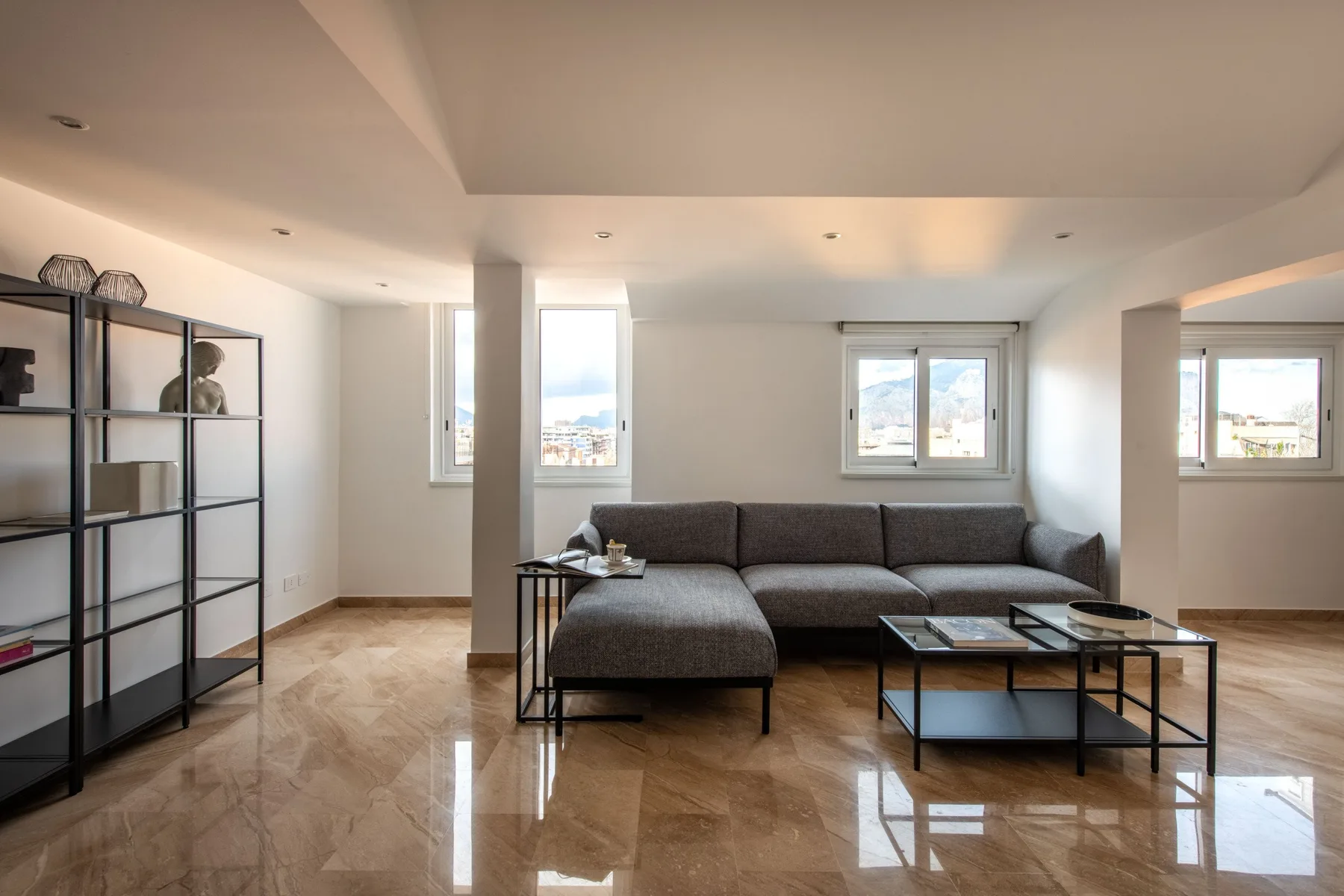 A bright living room with a sectional sofa, shelving, and large windows.