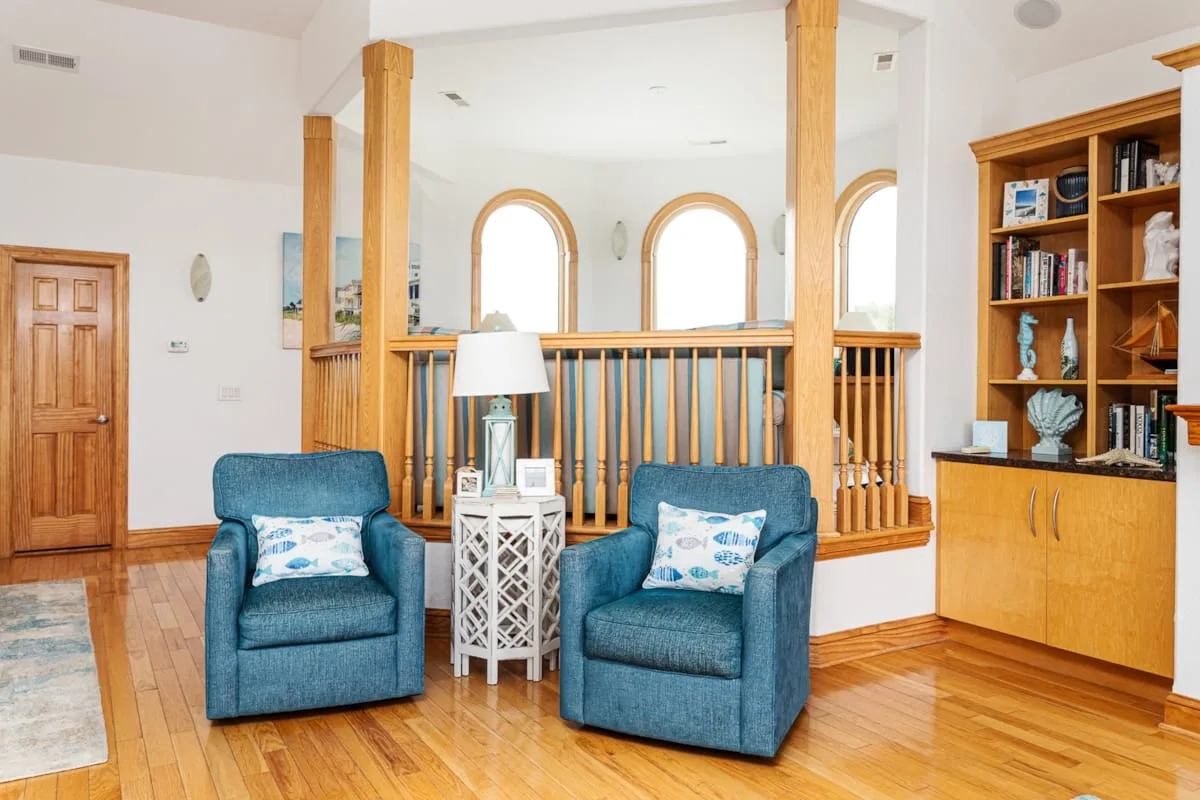 Una luminosa sala de estar con dos sillones azules junto a una barandilla de madera y una estantería.