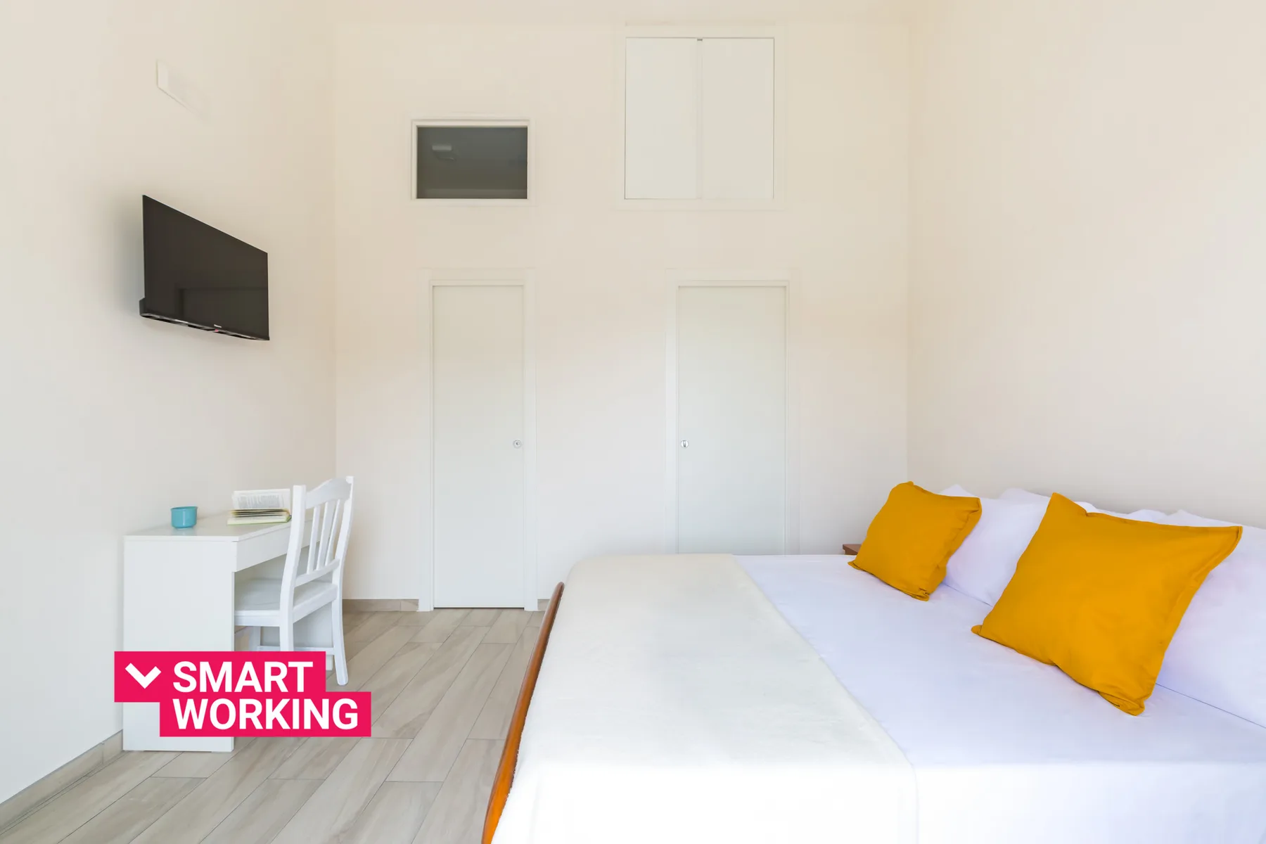 A bright bedroom with a bed, a wall-mounted television, and a small desk.