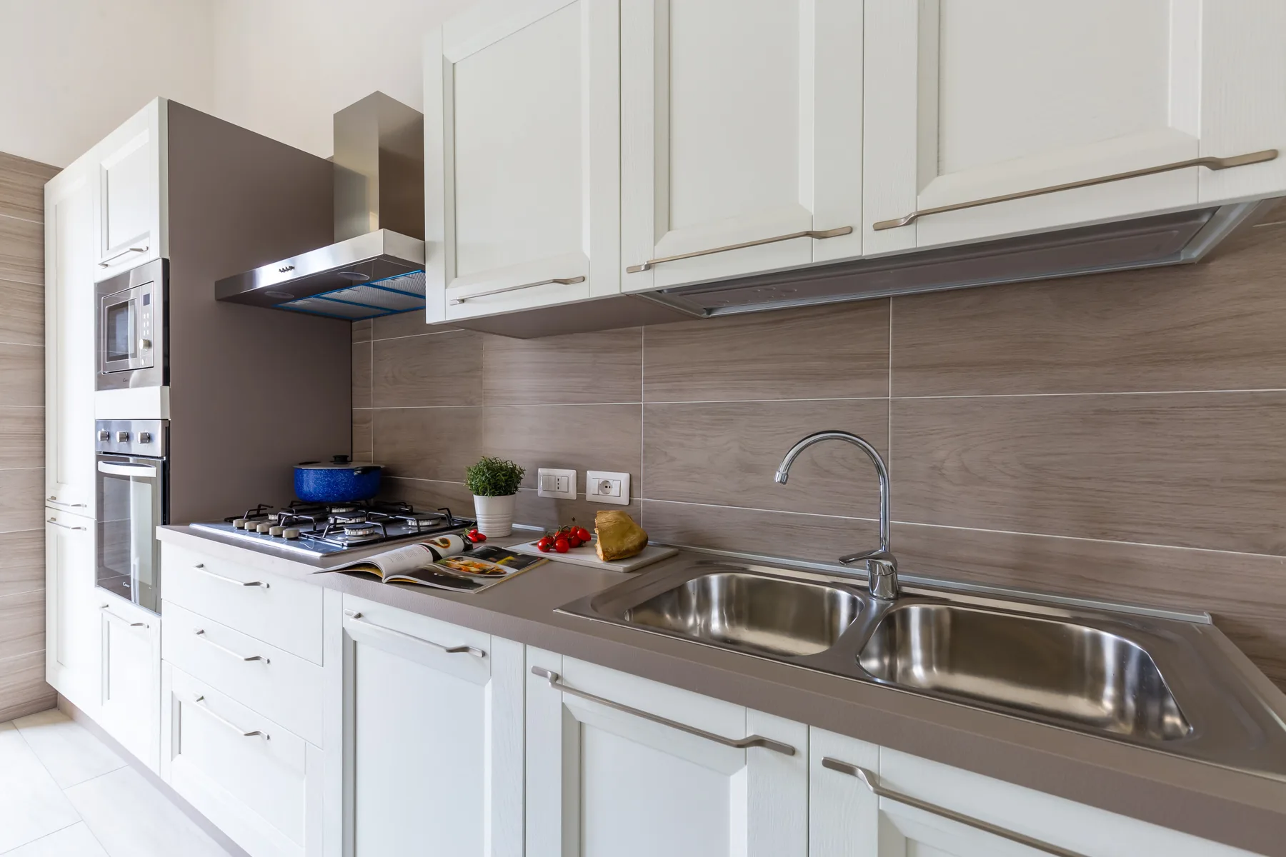 A modern kitchen with white cabinets, a cooktop, and a double-basin sink.