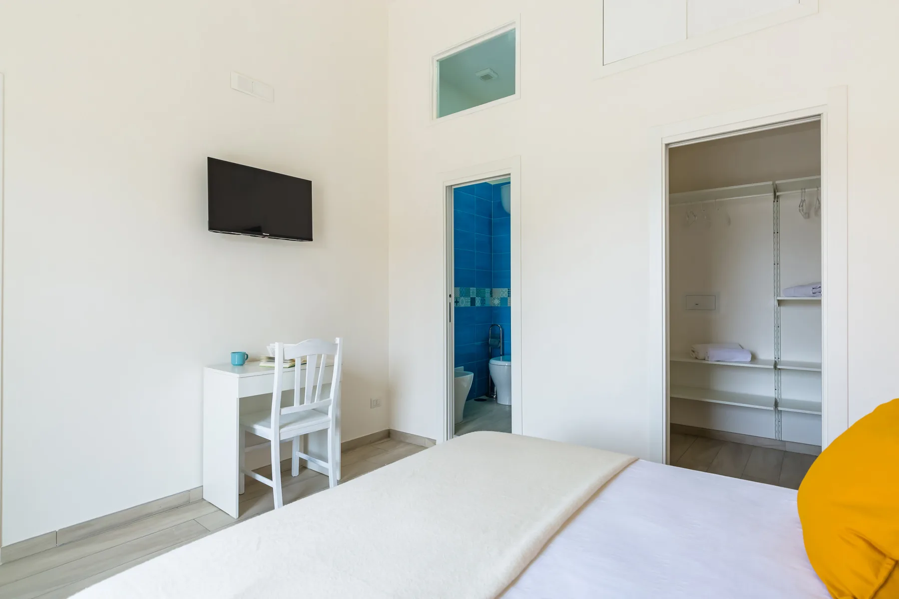 A bright bedroom with a bed, desk, and open bathroom doorway.