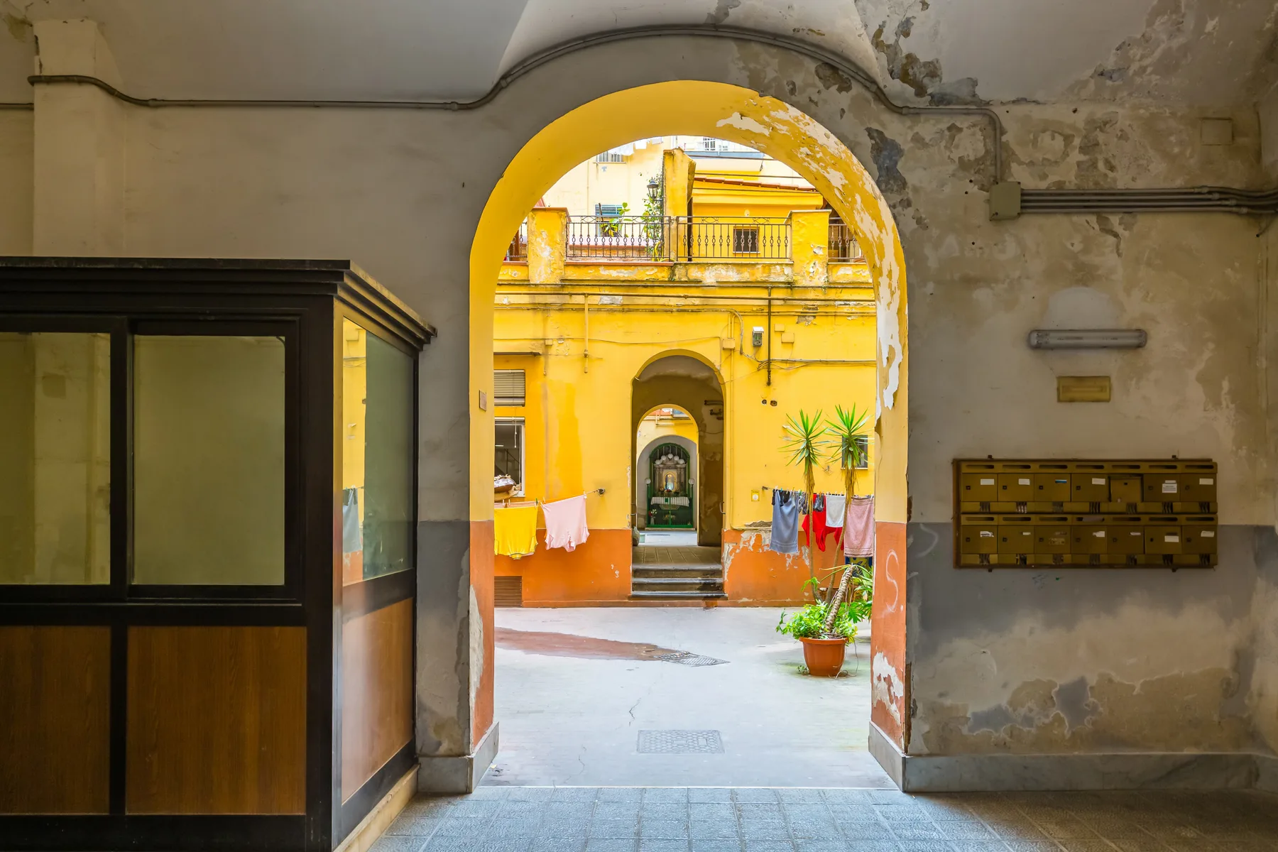 An arched entrance opens onto a colorful courtyard with balconies and potted plants.