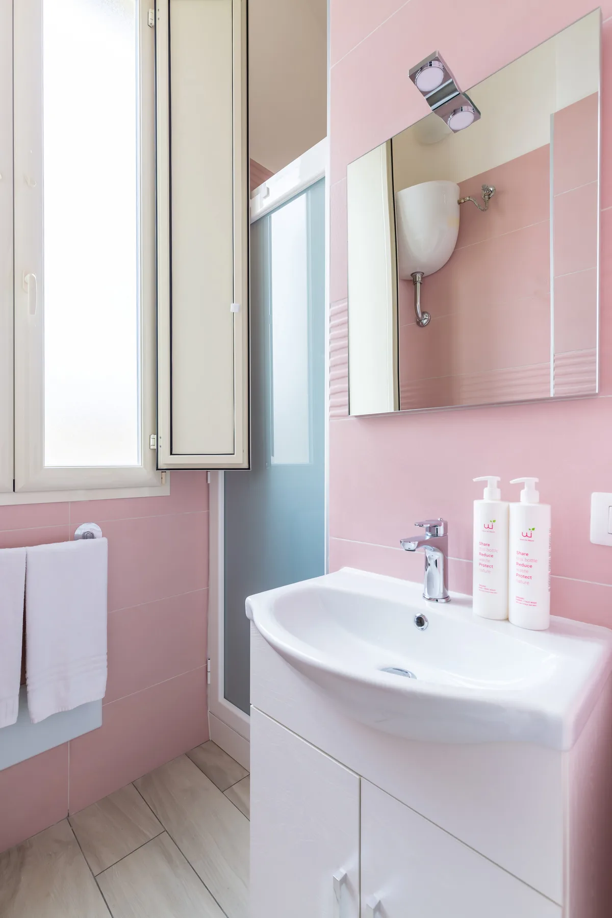 A pink bathroom features a white sink beneath a large wall mirror.