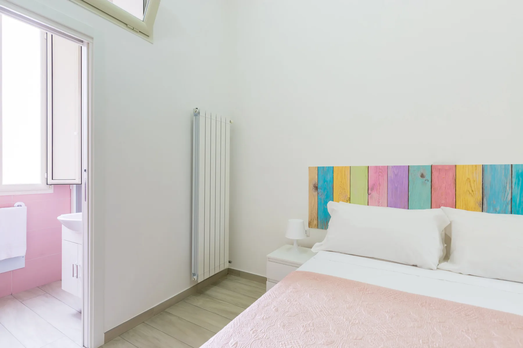 A bedroom with white bedding and a colorful plank headboard.