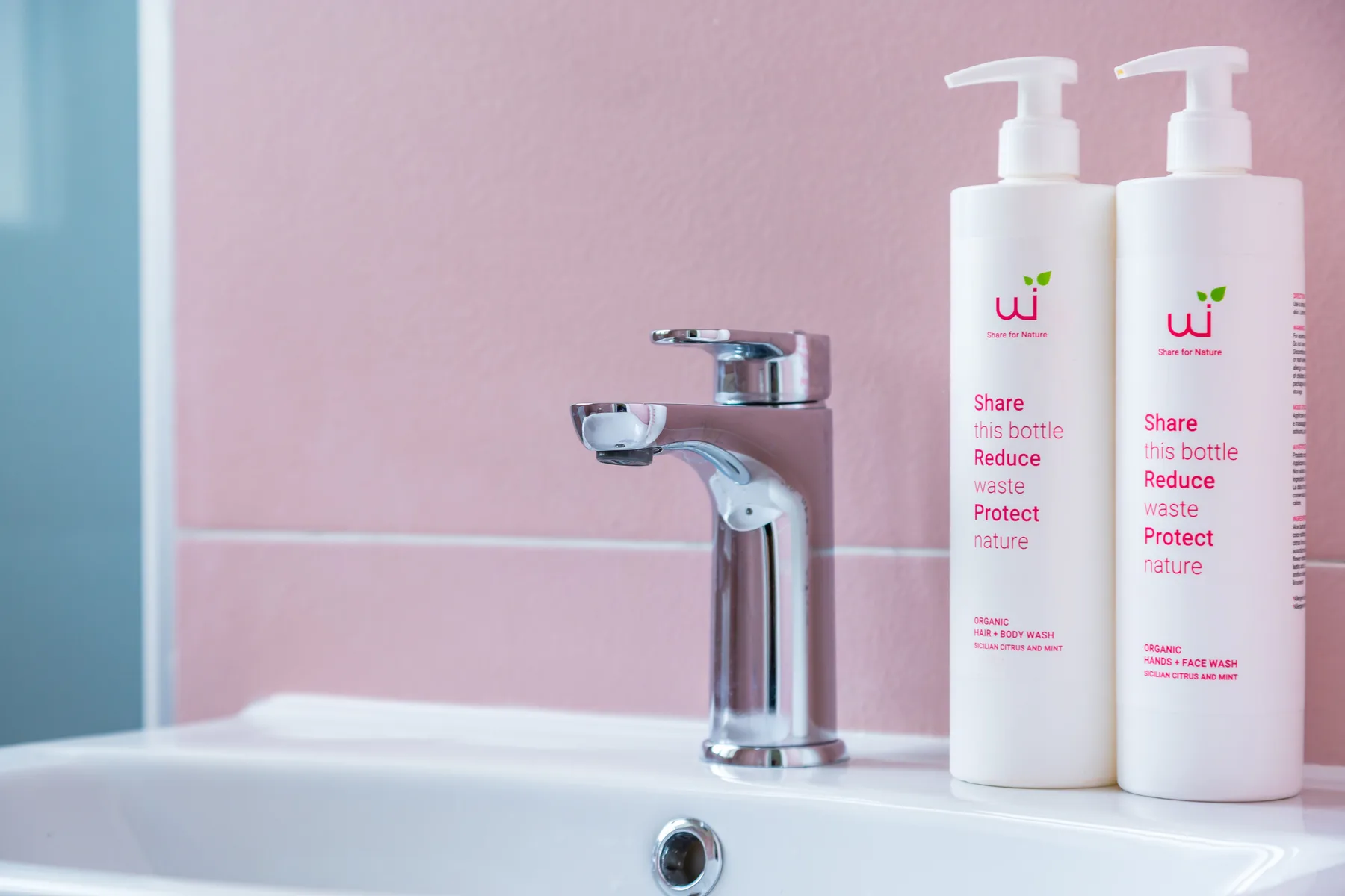 A bathroom sink with a chrome faucet and two pump bottles against a pink wall.