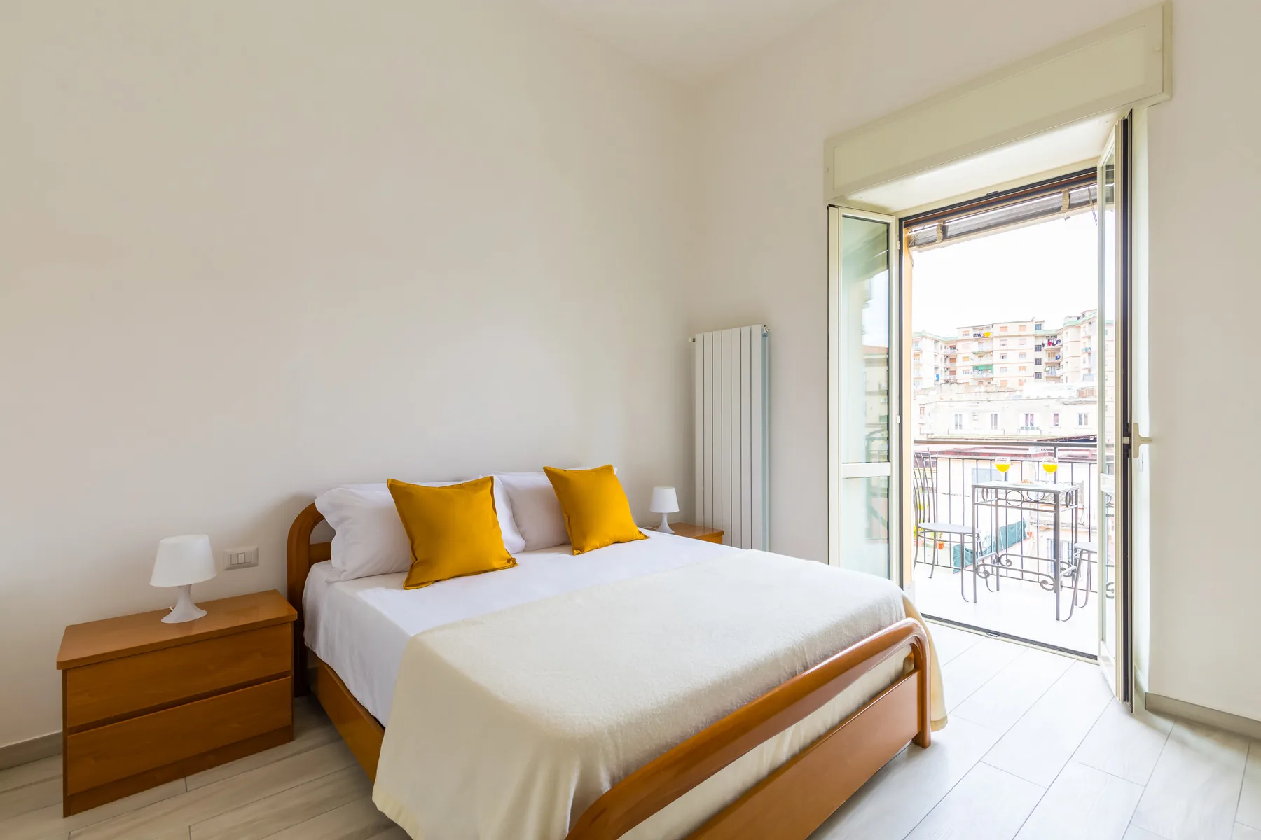 A bright bedroom with a made bed beside an open balcony door.