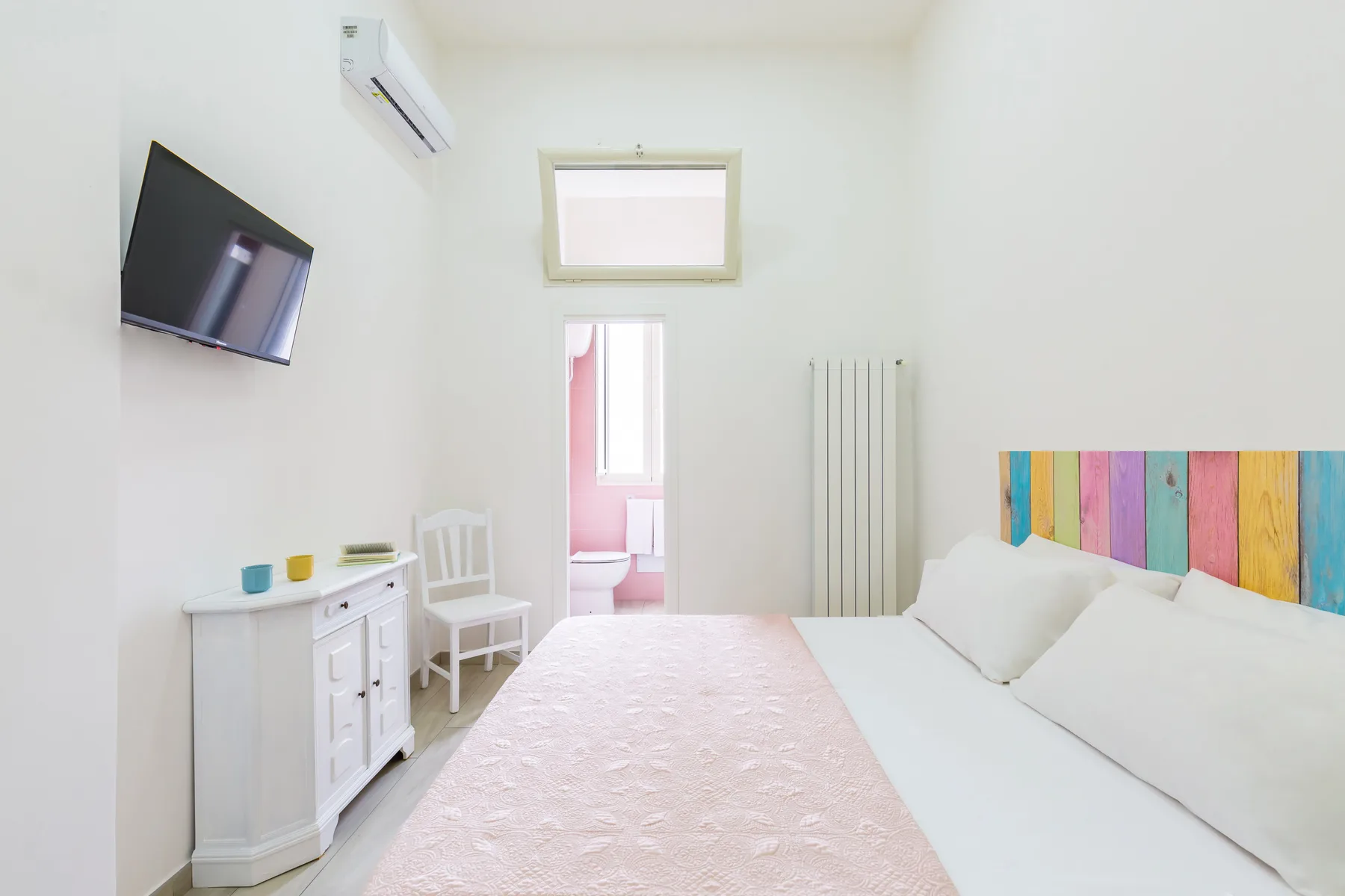 A bright bedroom with a bed, colorful headboard, and a small dresser.