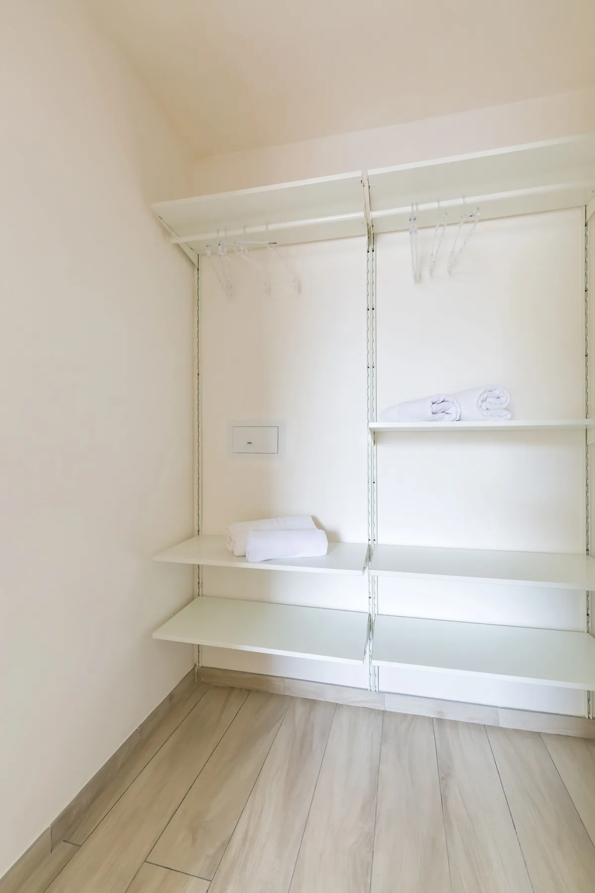An empty closet with white shelving and a light wood floor.