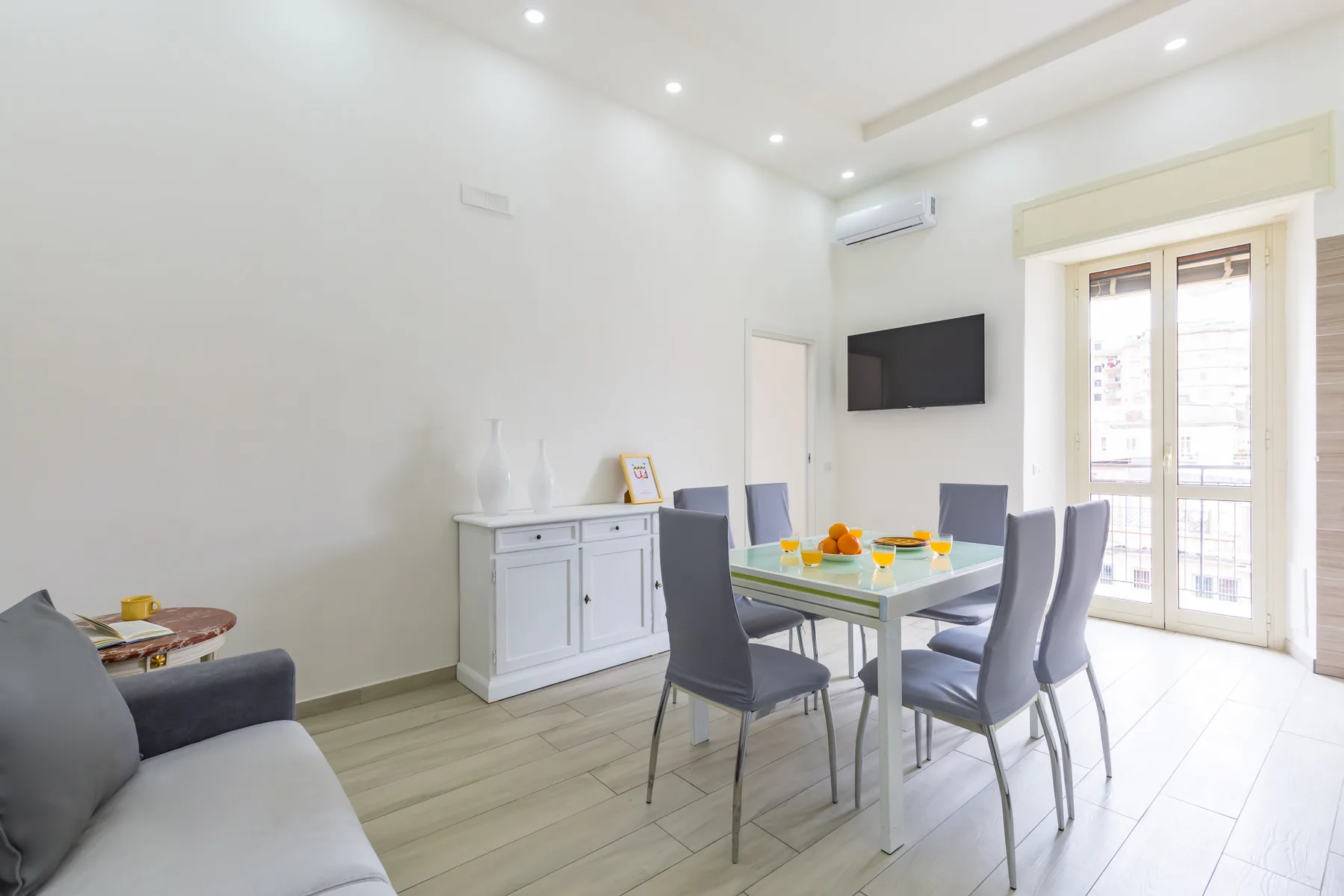 A bright dining area with a table and chairs beside a sofa and balcony doors.