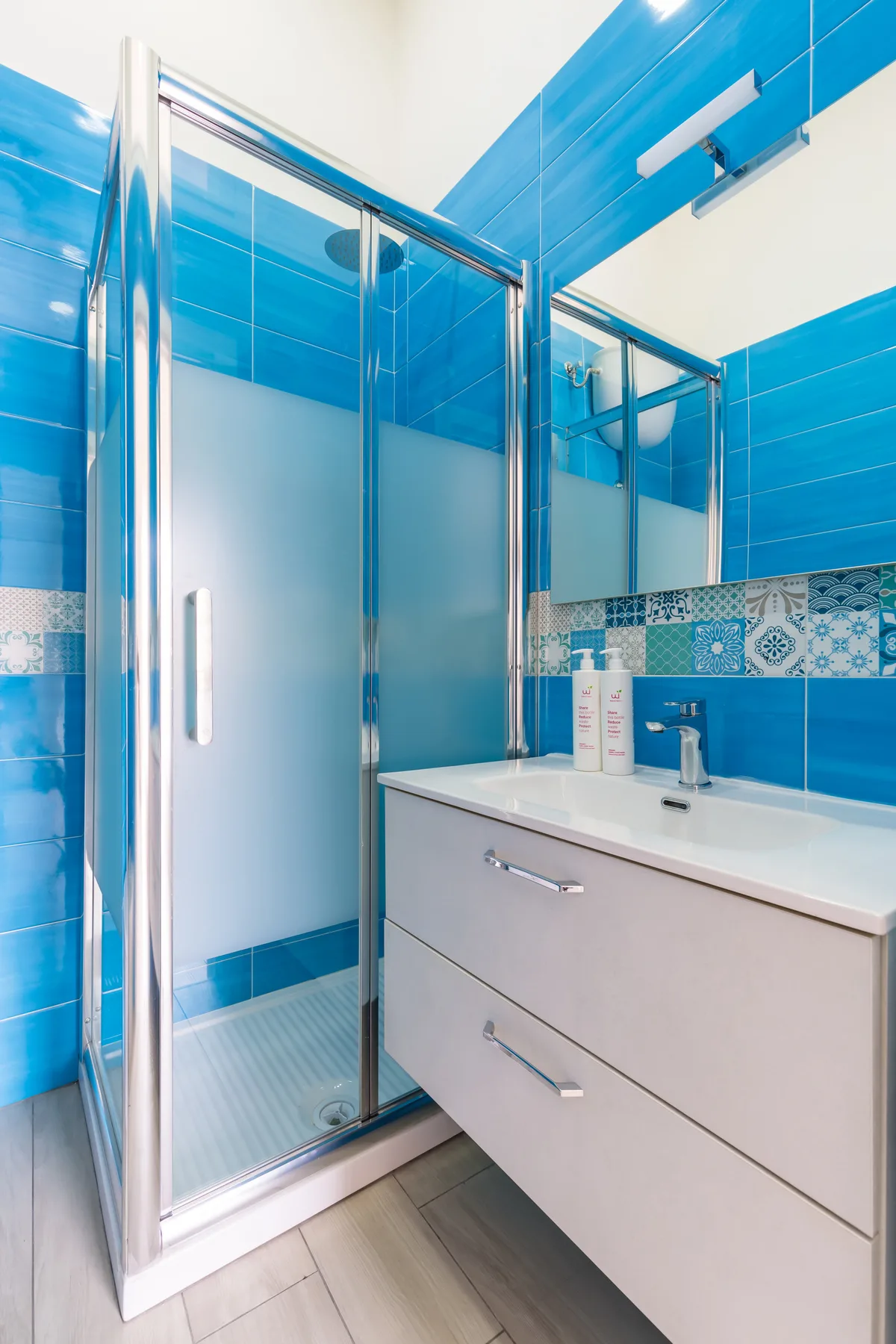 A blue-tiled bathroom with a glass shower and a white vanity.