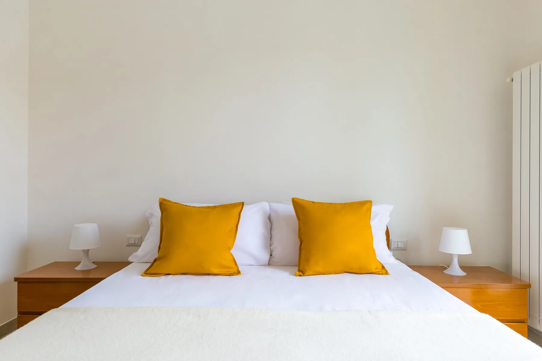 A bedroom with white bedding and two golden accent pillows.