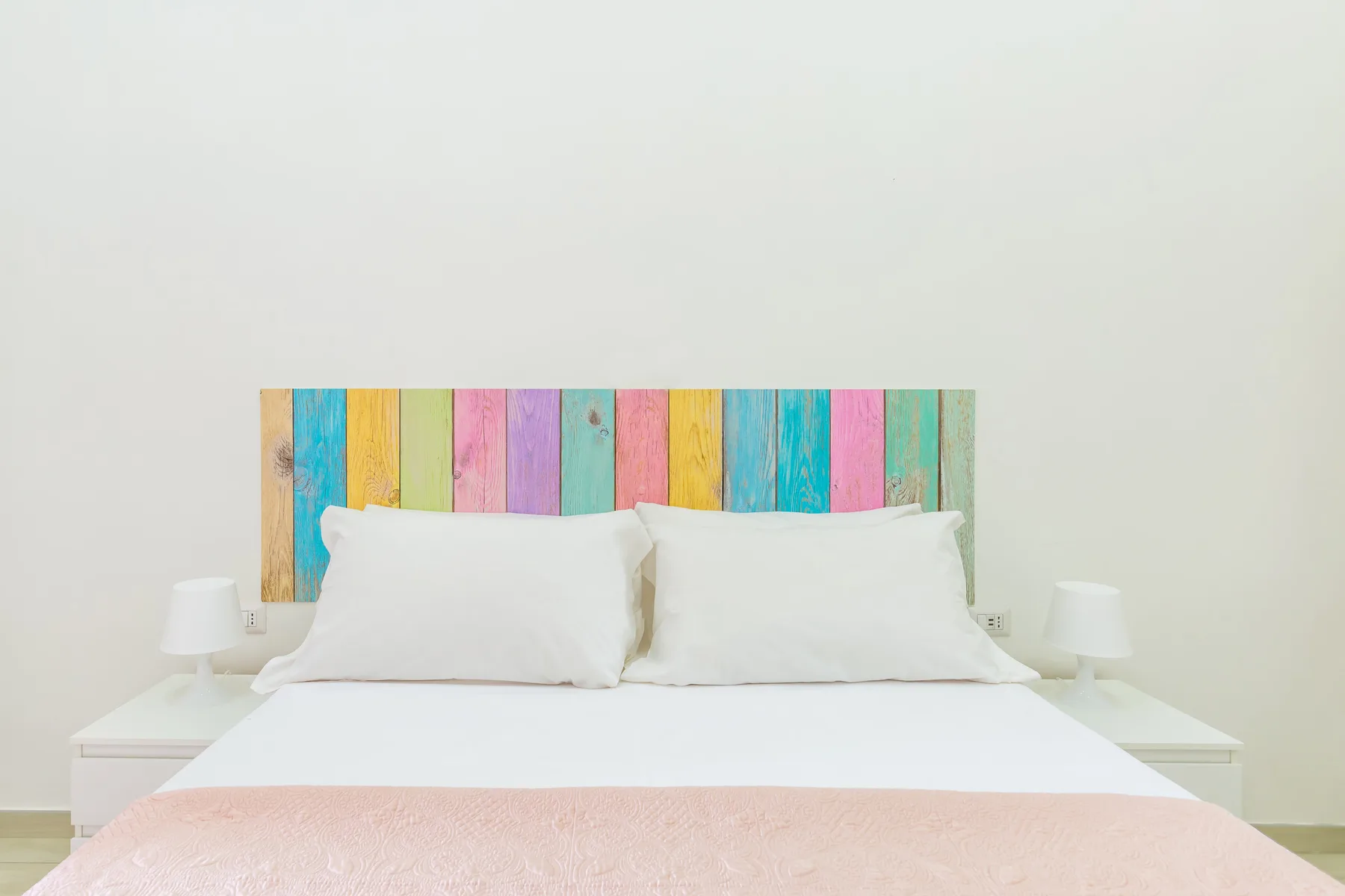 A bright bedroom with a white bed and a colorful striped headboard.