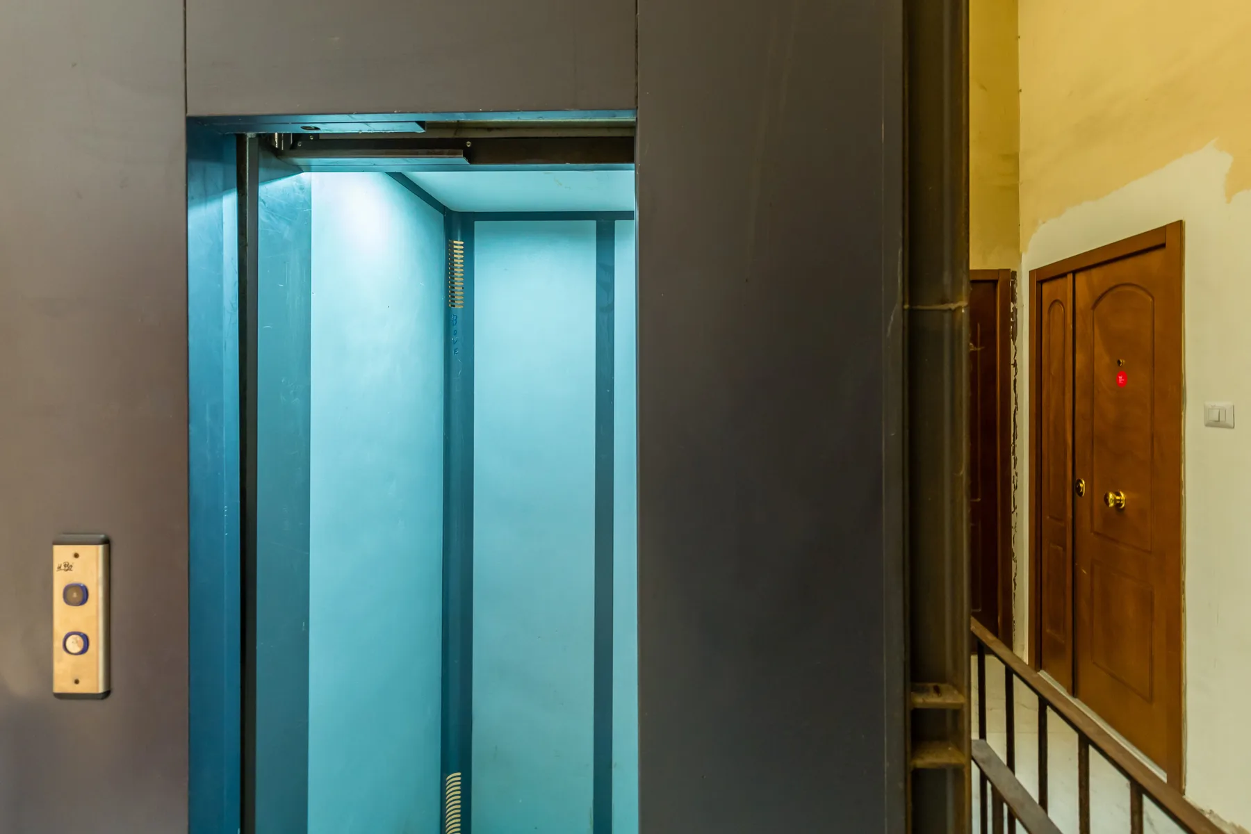 An elevator with blue interior doors opens beside a hallway.