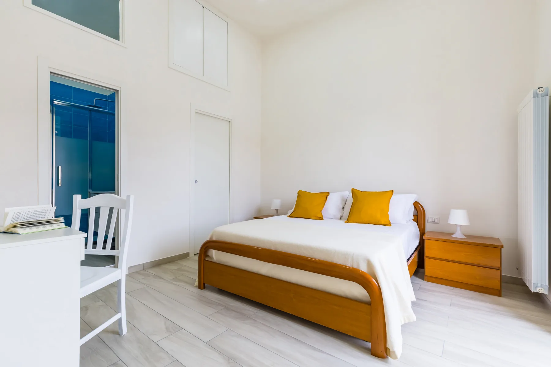 A bright bedroom with a wooden bed dressed in white linens and yellow pillows.