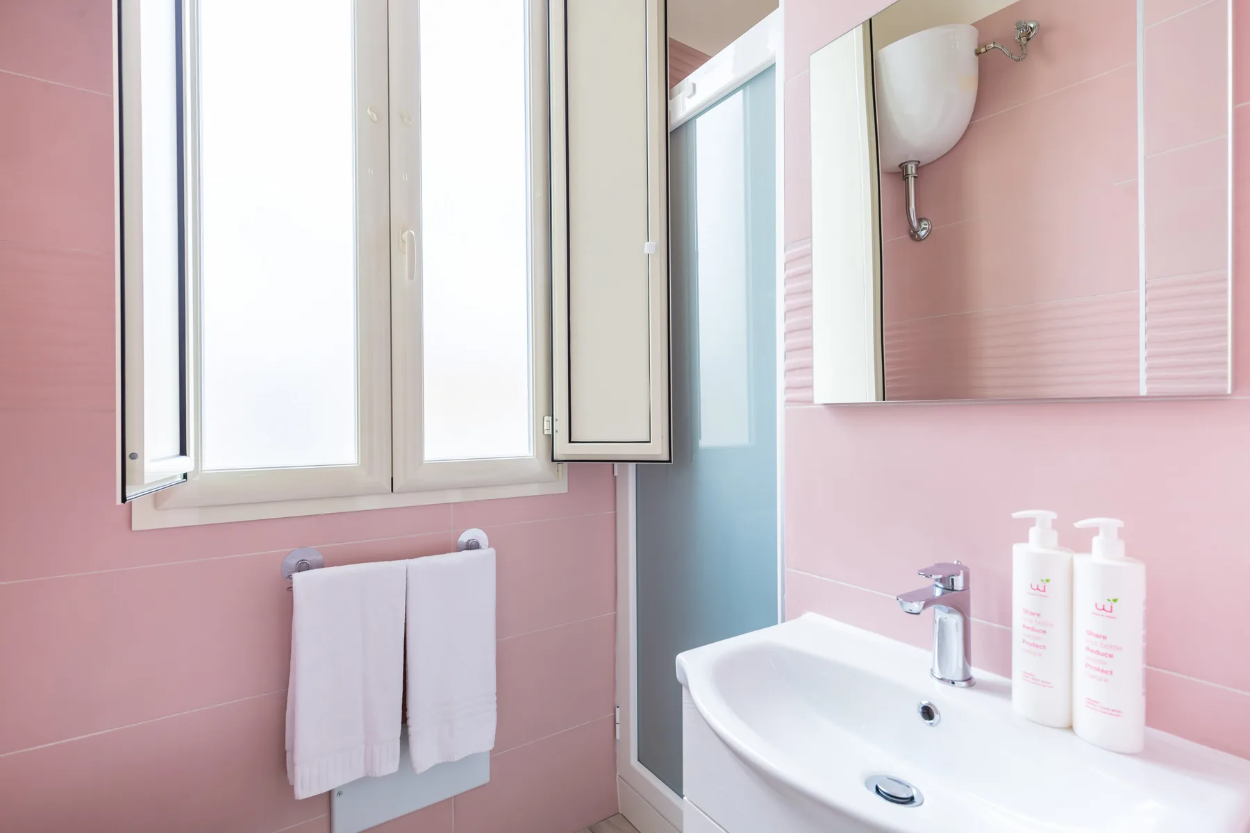 A pink-tiled bathroom with a sink and open window.