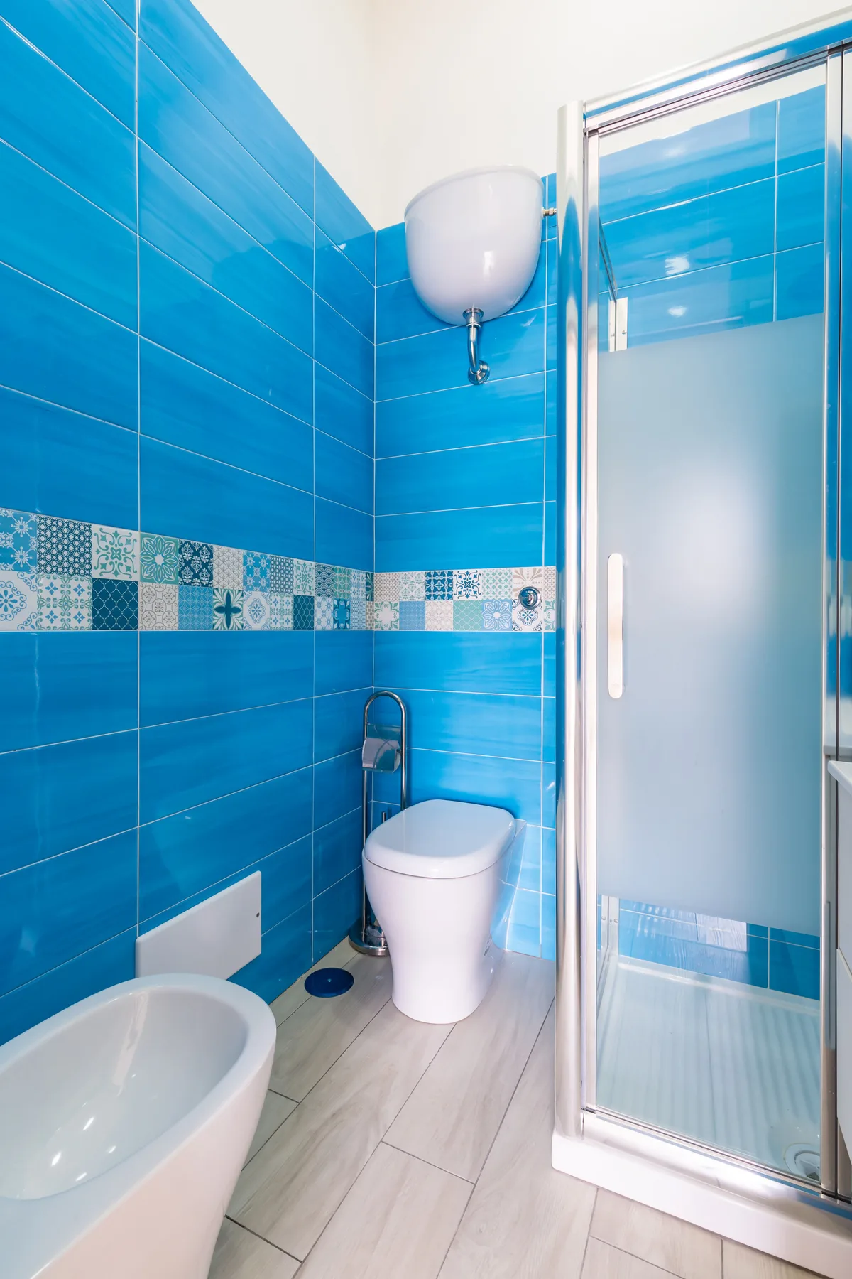 A blue-tiled bathroom with a toilet and glass shower.