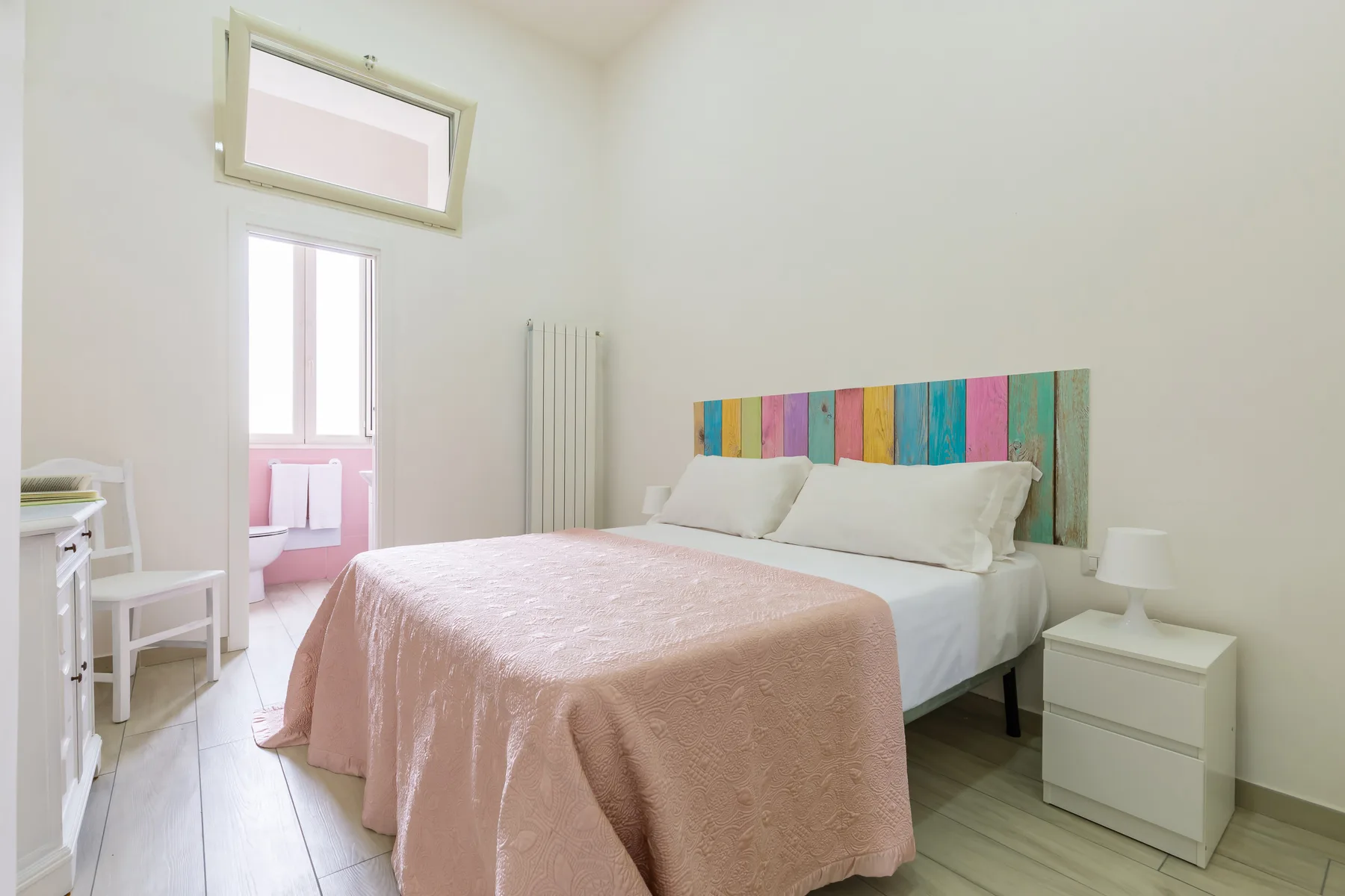 A bright bedroom with a double bed and colorful panel behind the headboard.