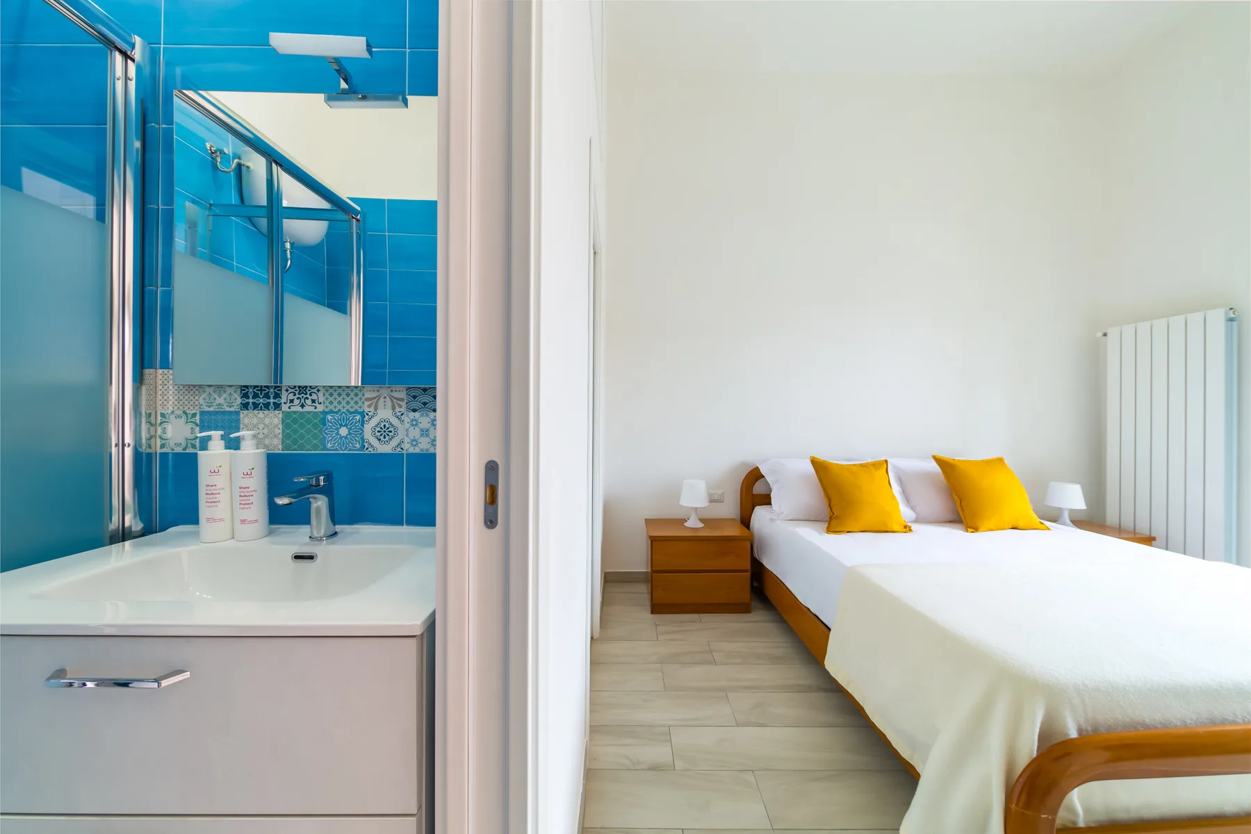 A bedroom with a white bed beside an adjoining bathroom.