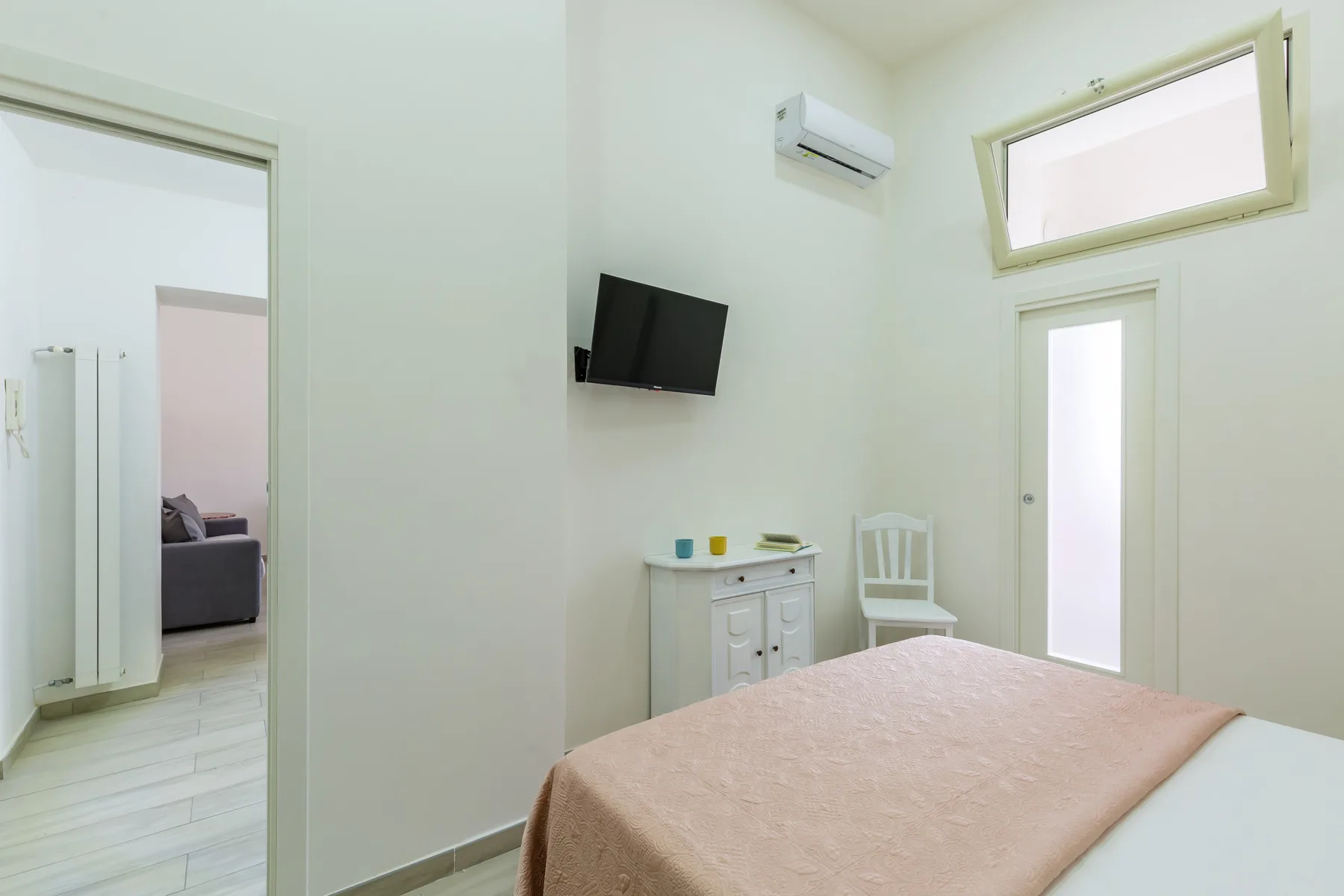 A bedroom with a bed, wall-mounted television, and a small dresser.