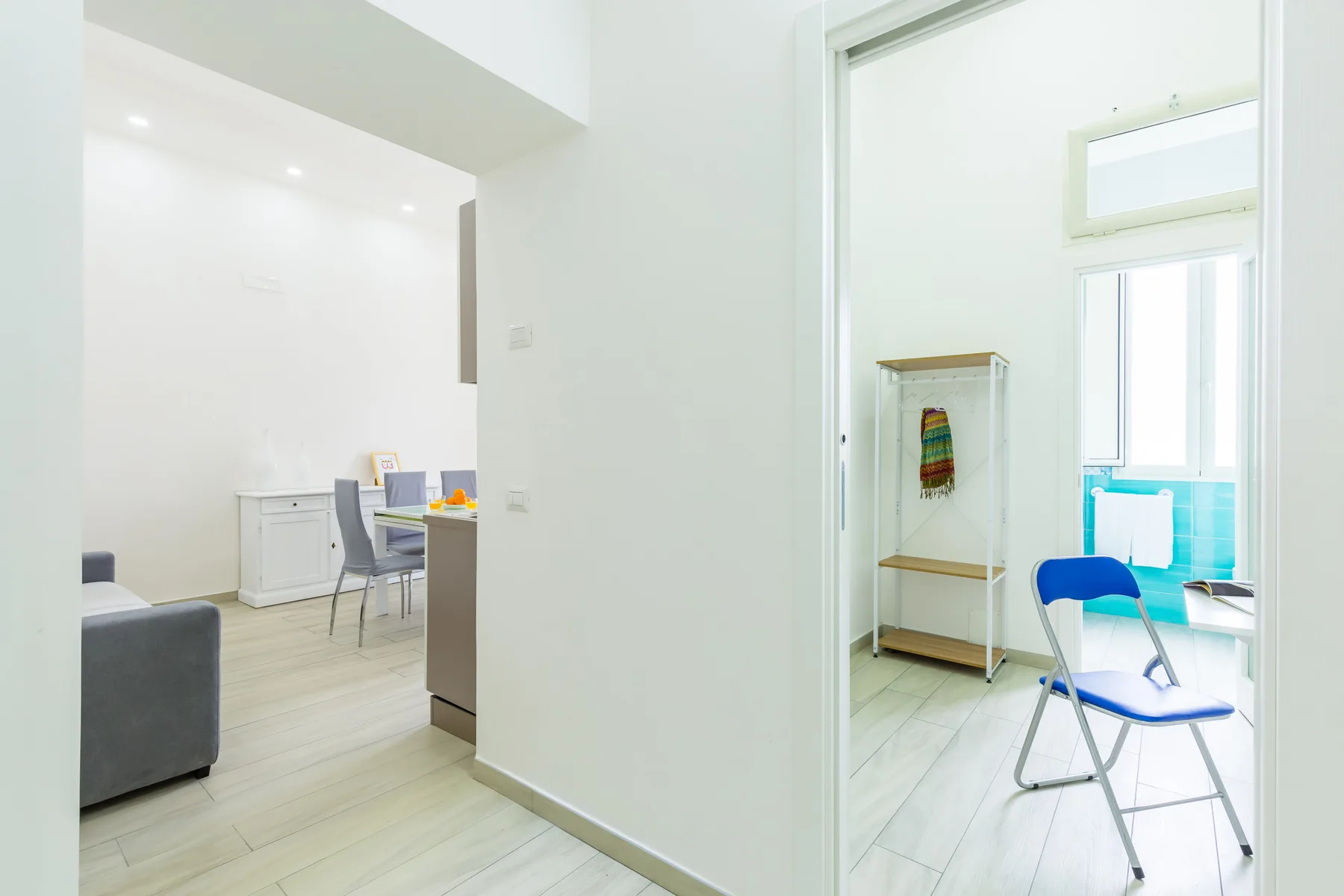 A bright interior shows a dining area beside a small room with a folding chair.