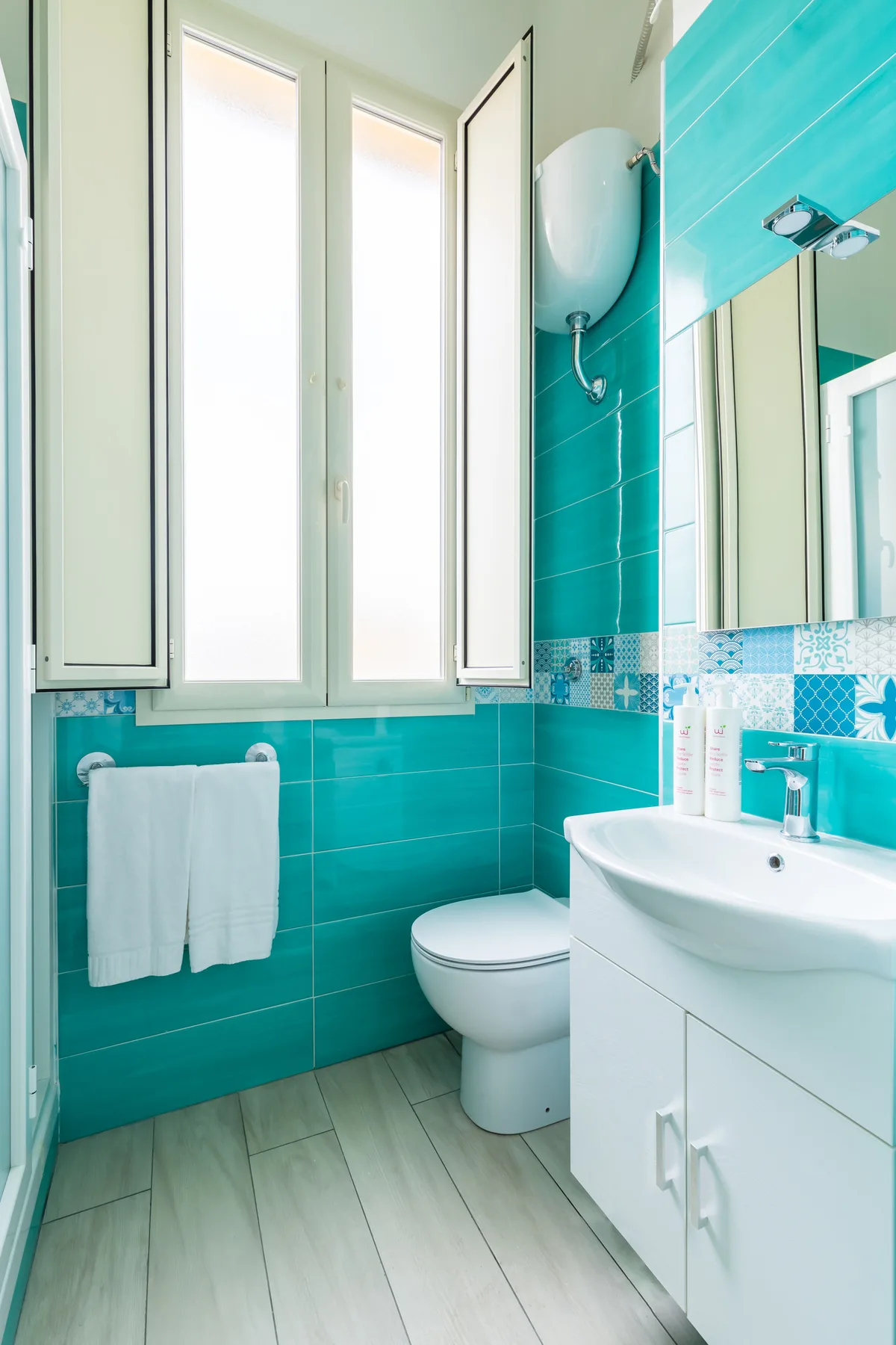A bright bathroom with turquoise wall tiles and a white sink.