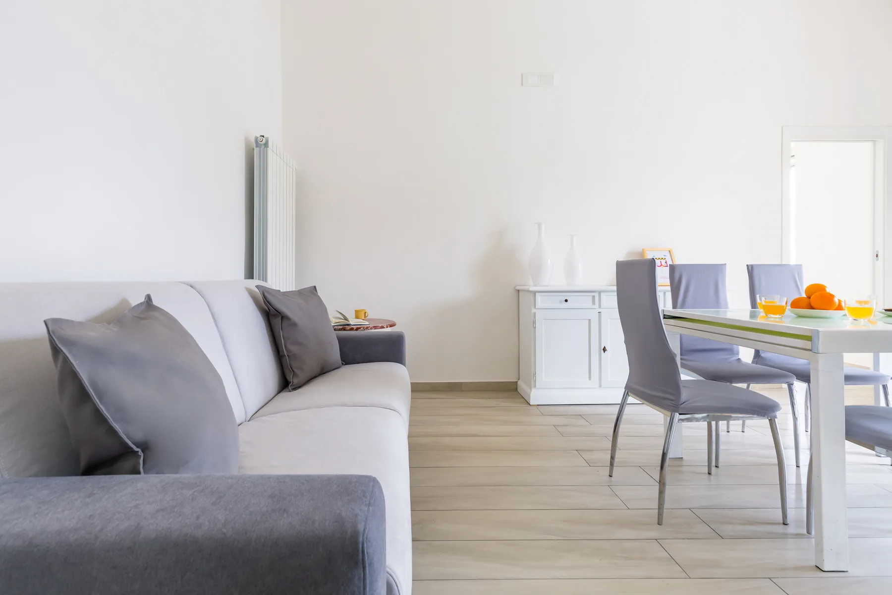 A bright living and dining area with gray seating and a dining table.