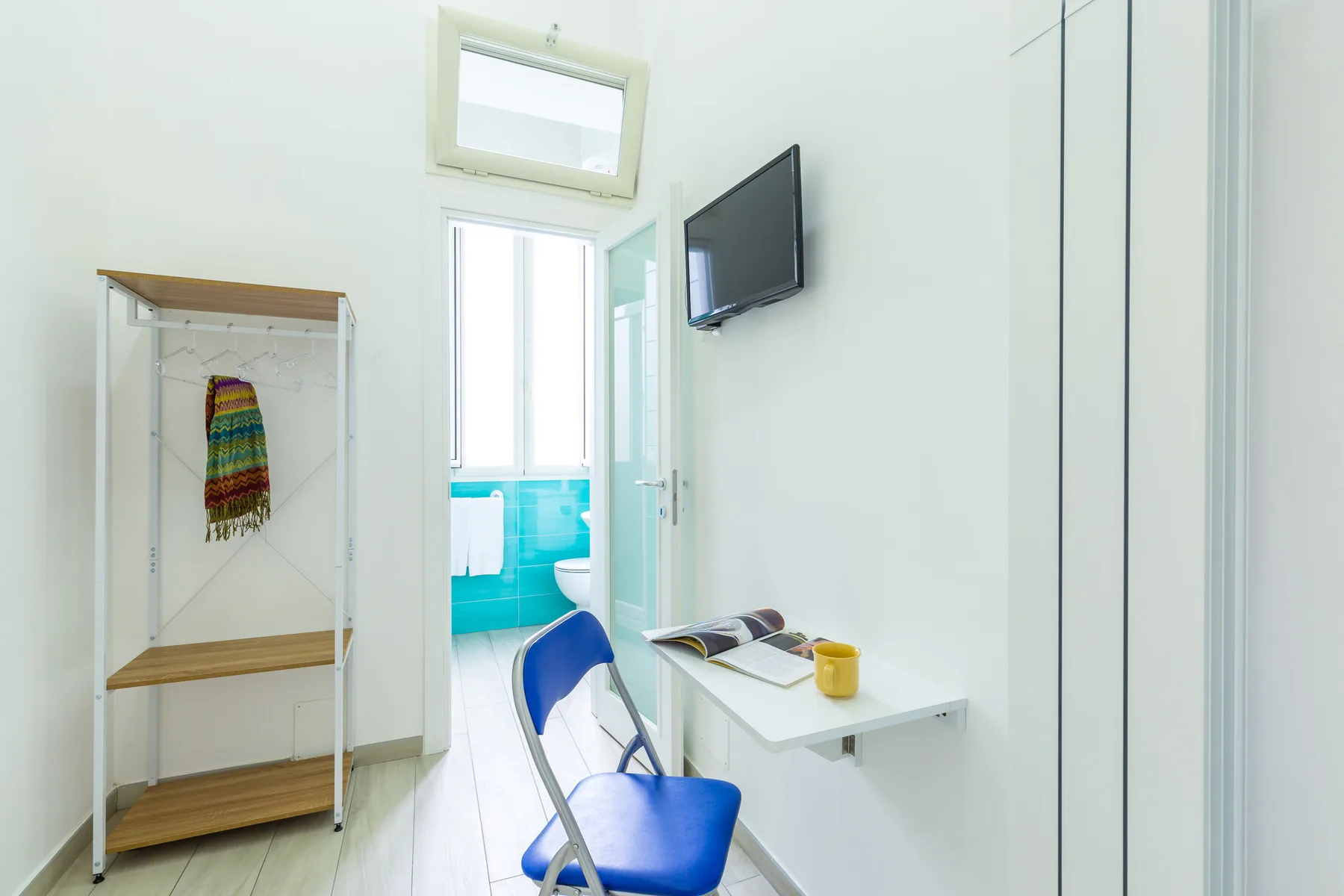A bright room with a desk, blue chair, wall-mounted television, and an open doorway.