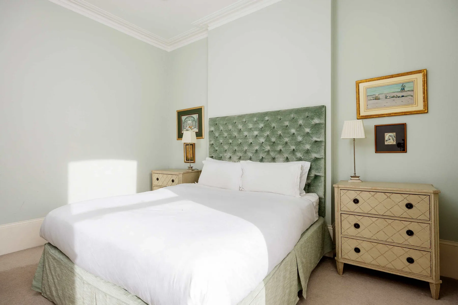 A bedroom with a white bed, green upholstered headboard, and bedside furnishings.