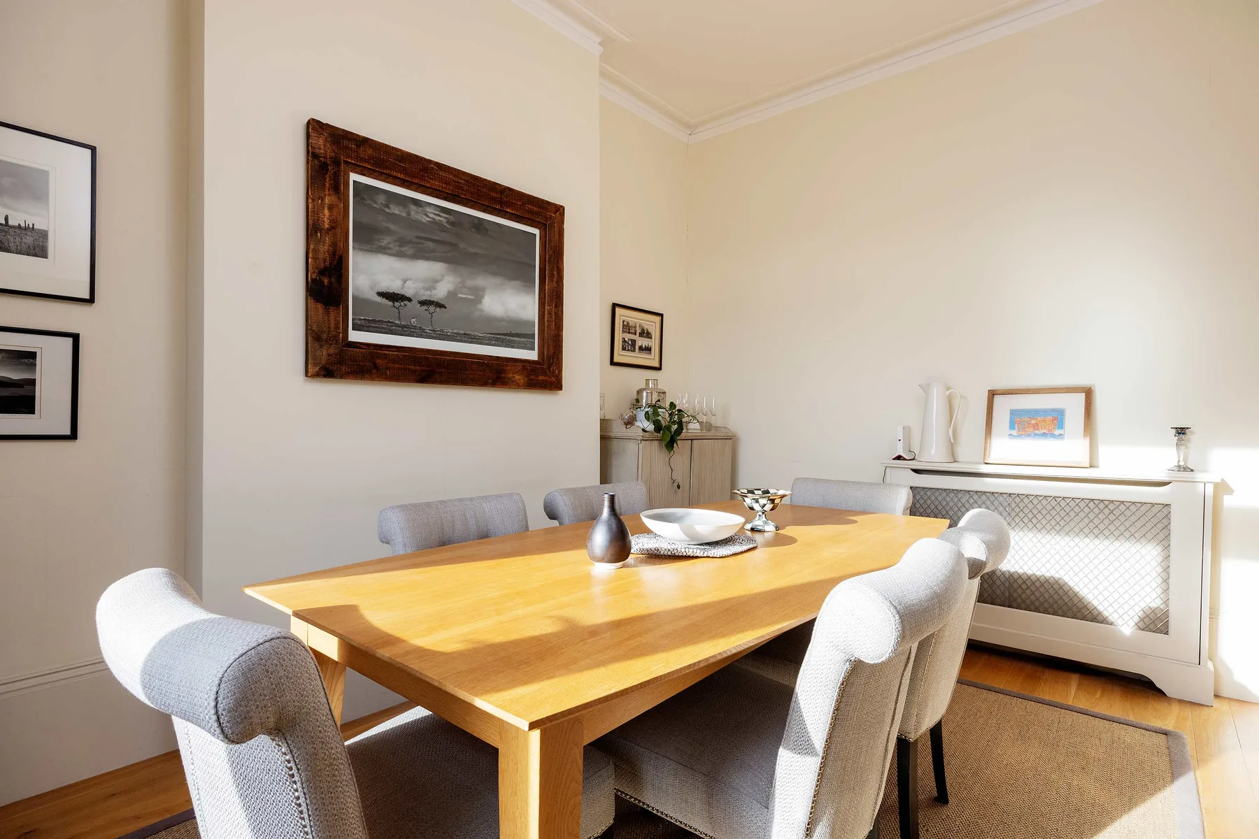 A dining room with a wooden table, upholstered seating, and framed artwork.