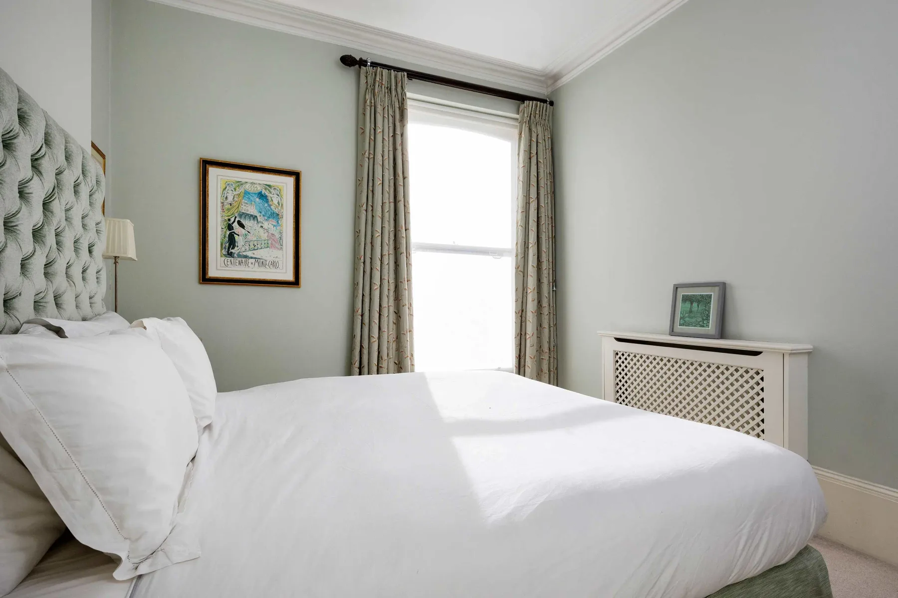 A bedroom with a bed beside a bright window and framed wall art.