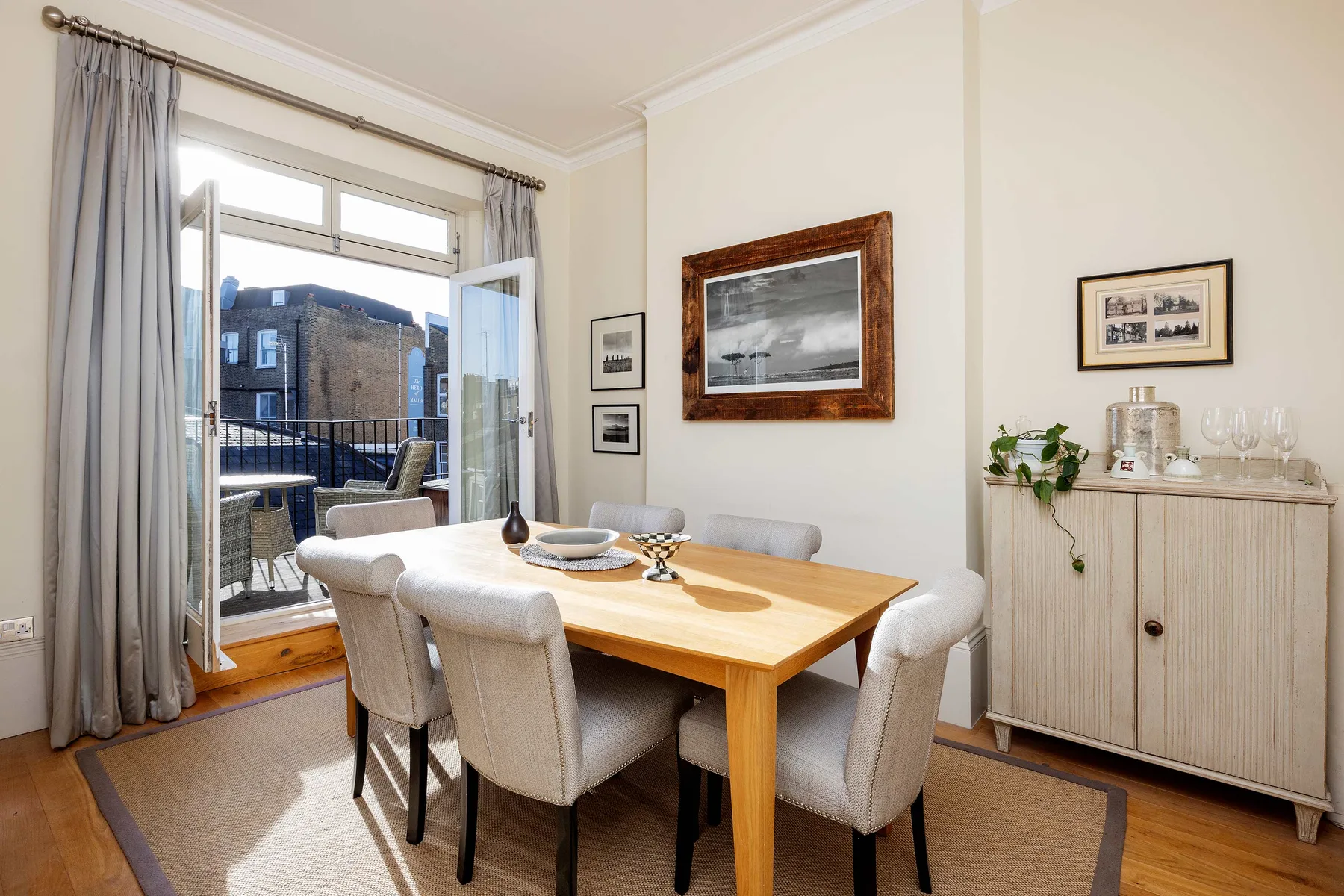 A dining area with a wooden table and upholstered seating beside open balcony doors.