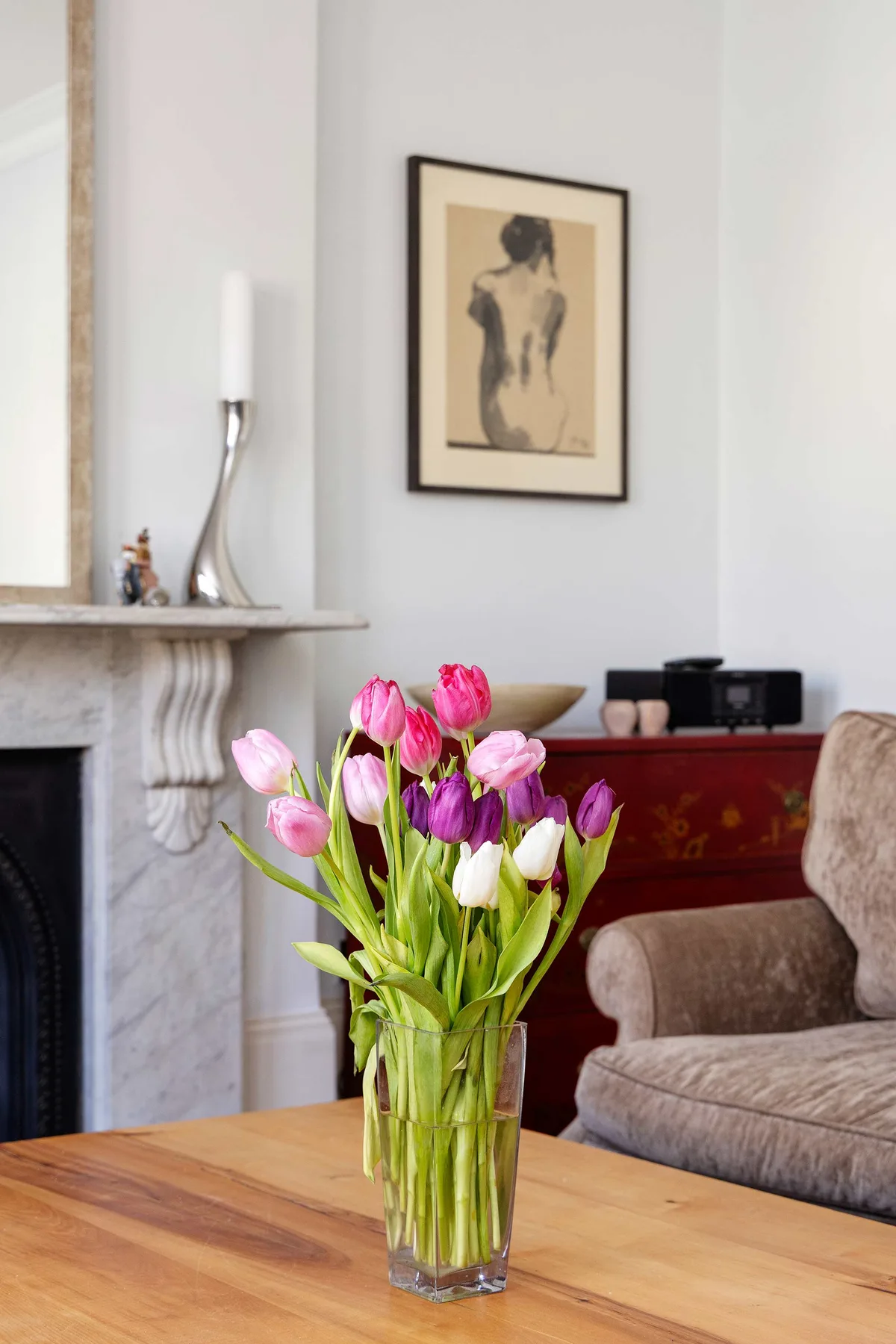 A living room with tulips in a glass vase on a wooden table.
