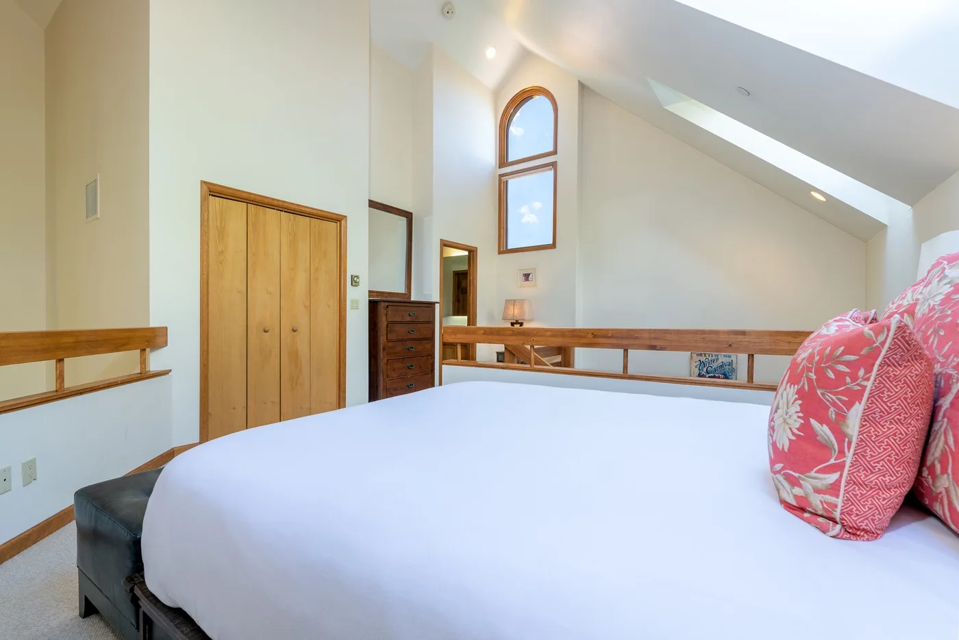 A bedroom with a large bed, red patterned pillows, and a high arched window.