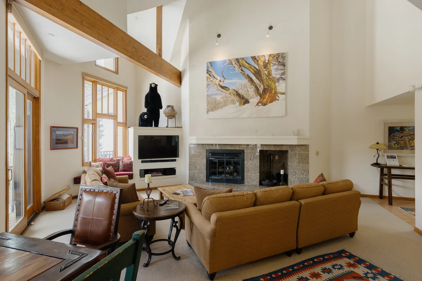 A bright living room with large windows, seating, and a fireplace.