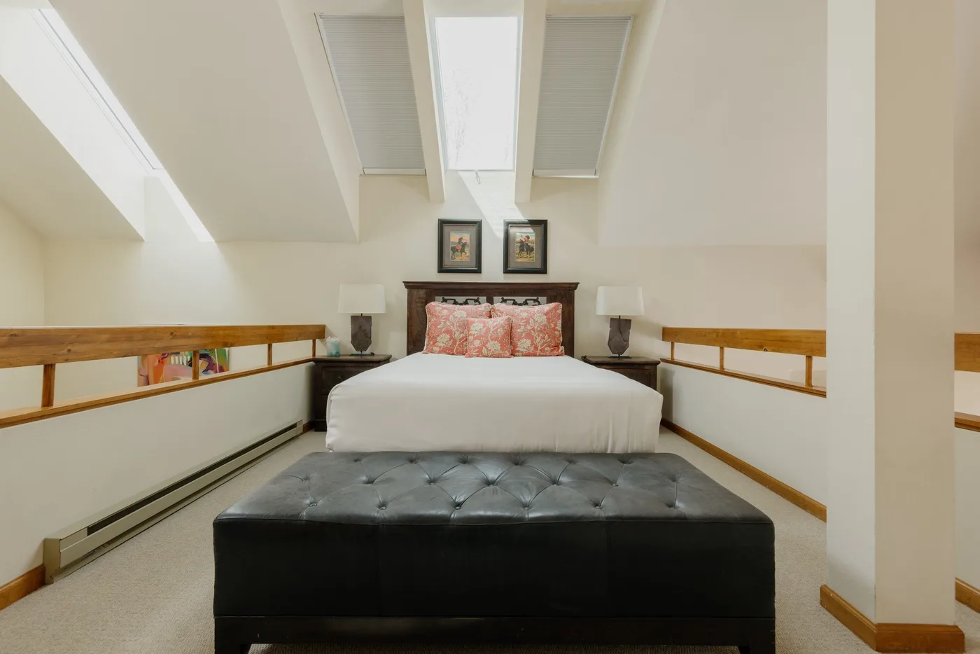 A bedroom with a bed beneath skylights and a dark upholstered bench at the foot.