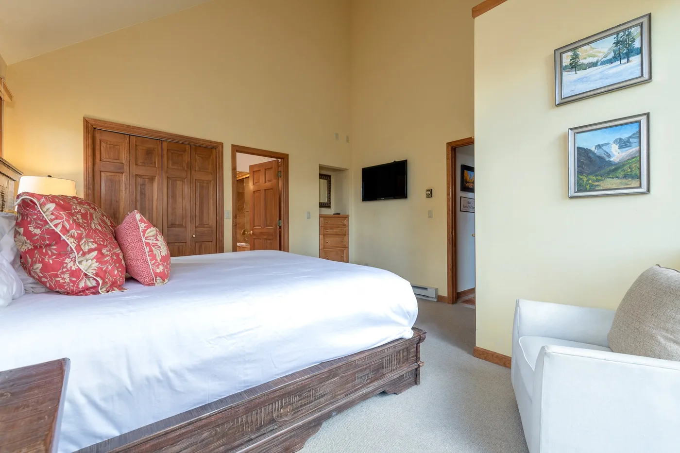 A bedroom with a large bed, patterned pillows, and a wall-mounted television.