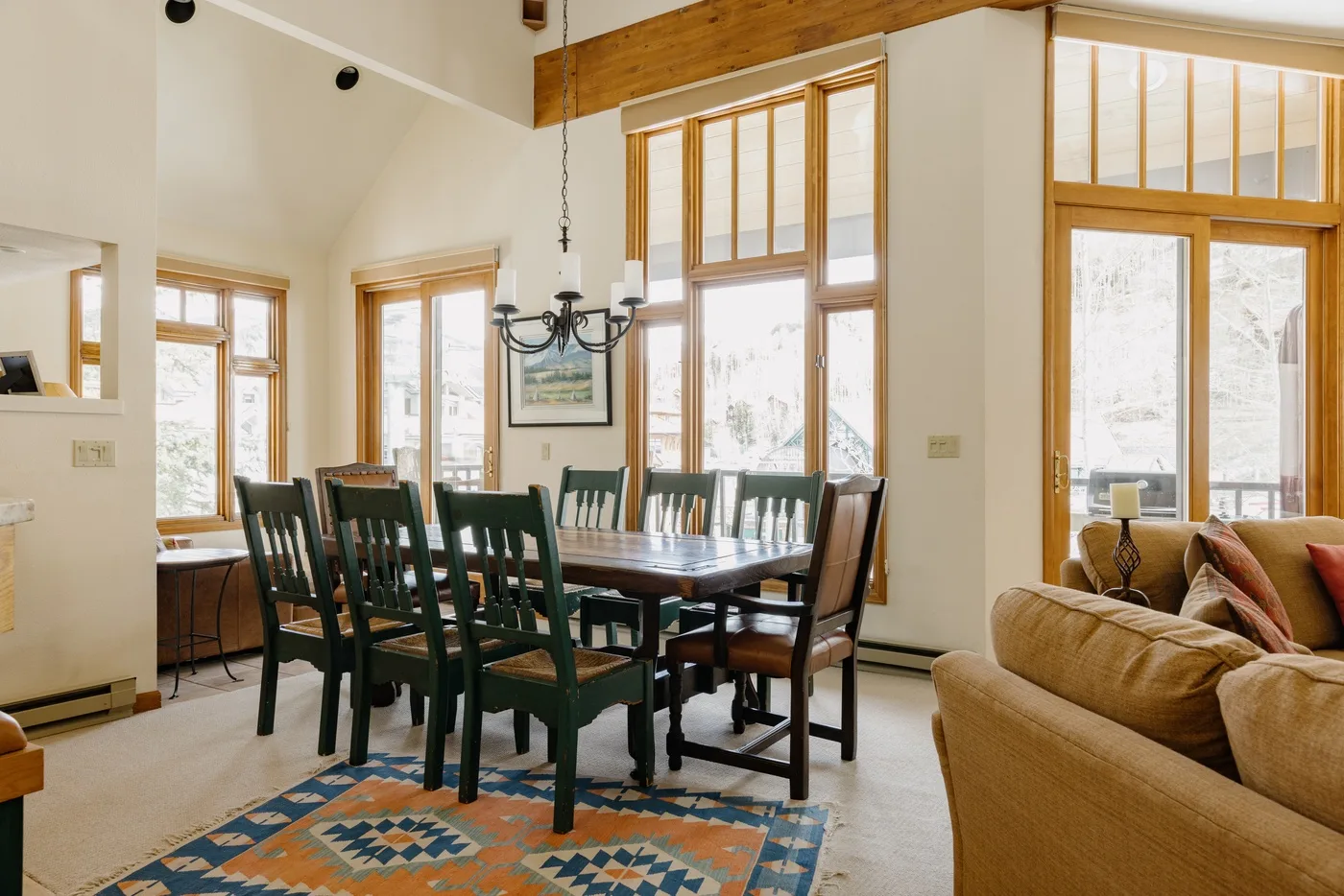 A dining area with a long table and dark chairs beside large windows.