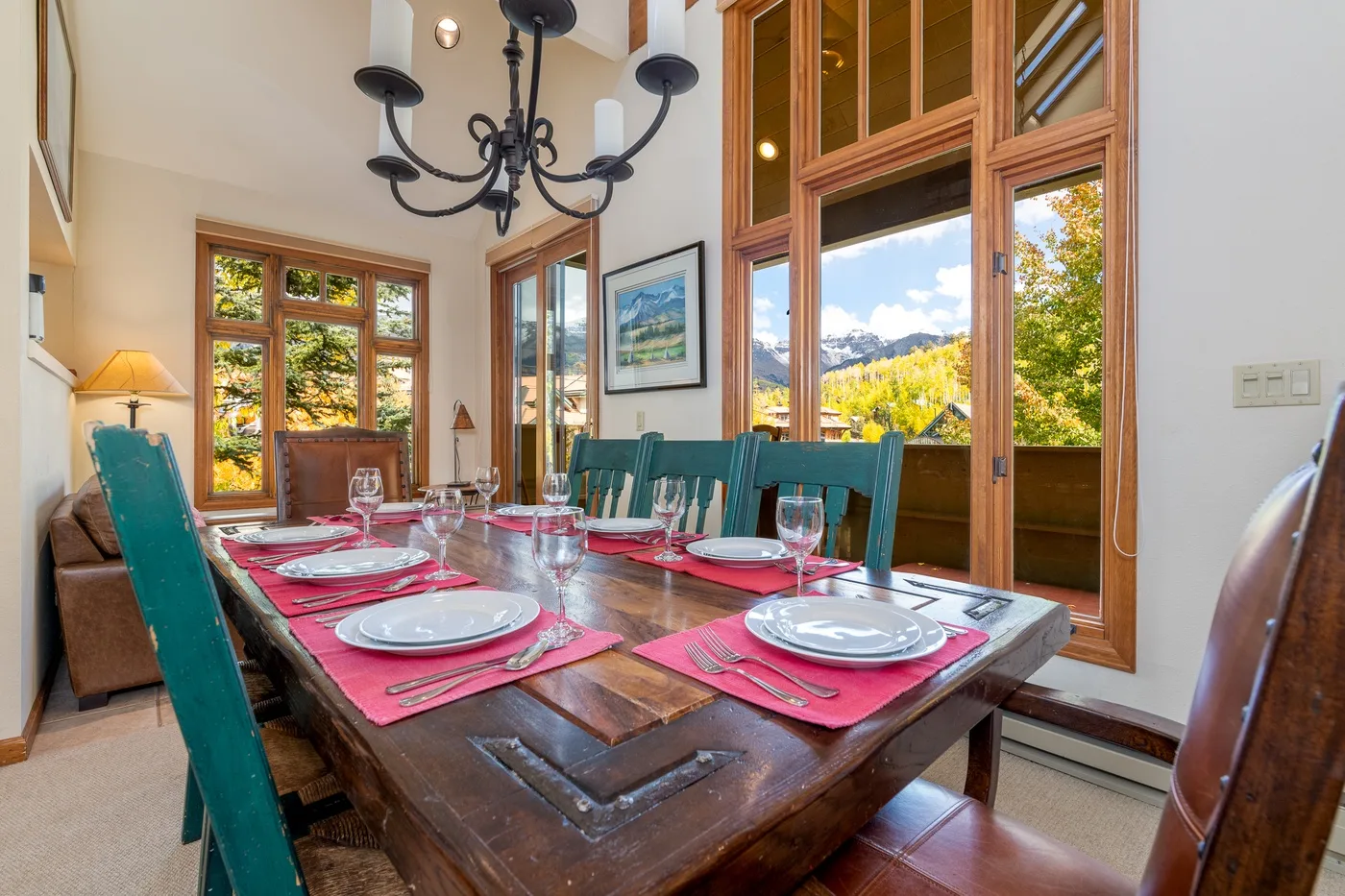 A dining room with a long table set with plates beside large windows.