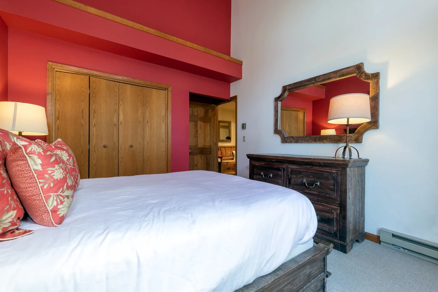 A bedroom with a bed, patterned pillows, and a dark dresser beneath a mirror.