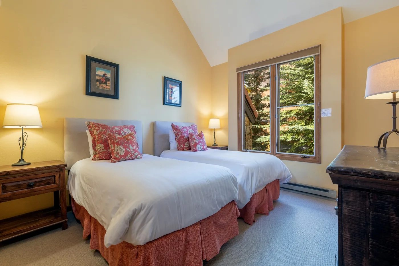 A bedroom with two beds, bedside tables, and a large window.