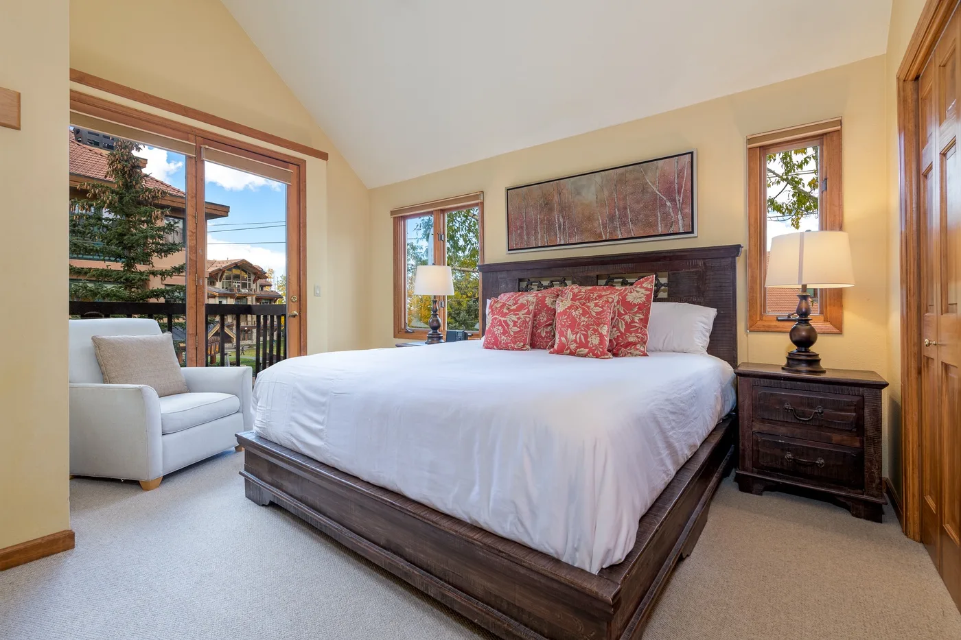 A bright bedroom with a large bed and windows overlooking trees.