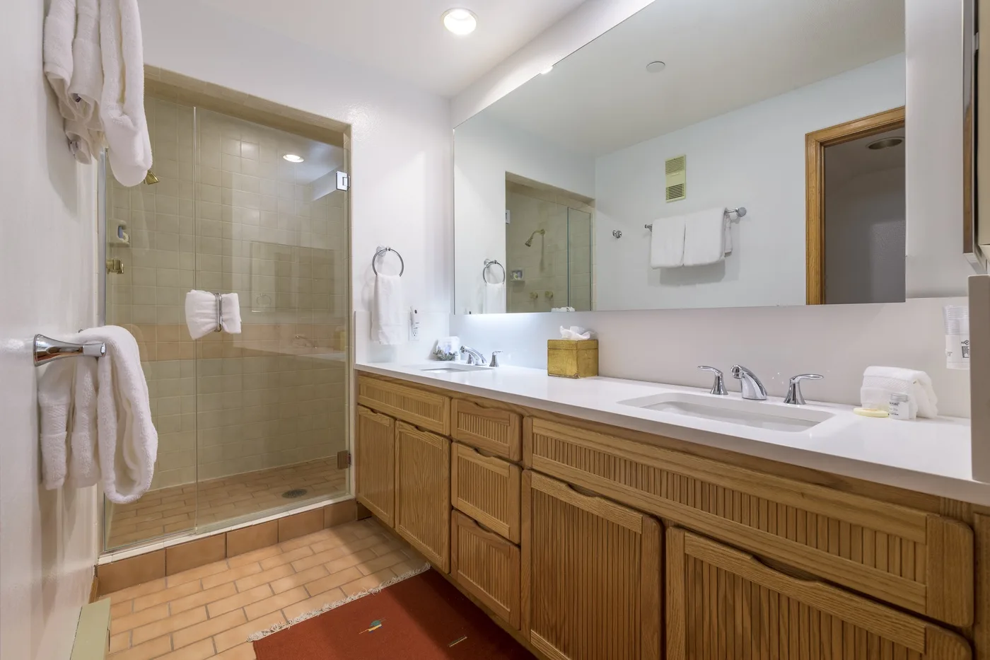 A bathroom vanity with a wide mirror stands beside a glass-enclosed shower.