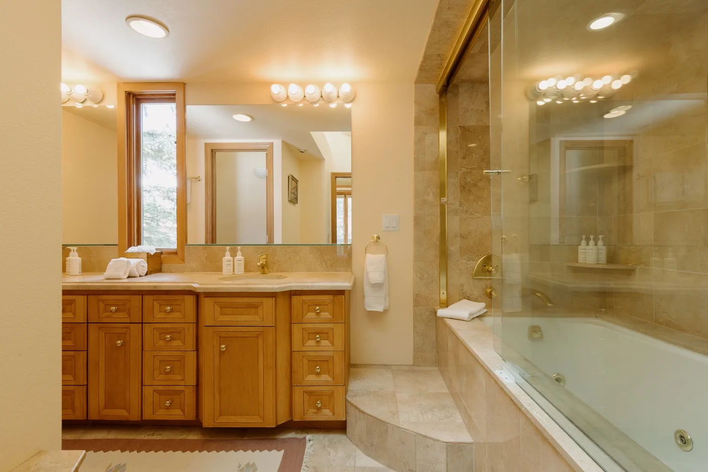 A bright bathroom features a long vanity beside a glass-enclosed bathtub.
