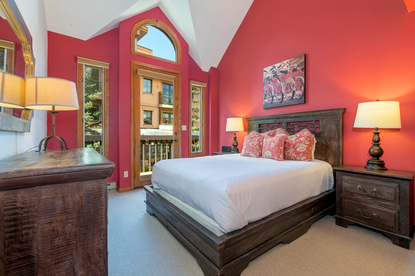 A bedroom with a wooden bed, colorful pillows, and bright red walls.
