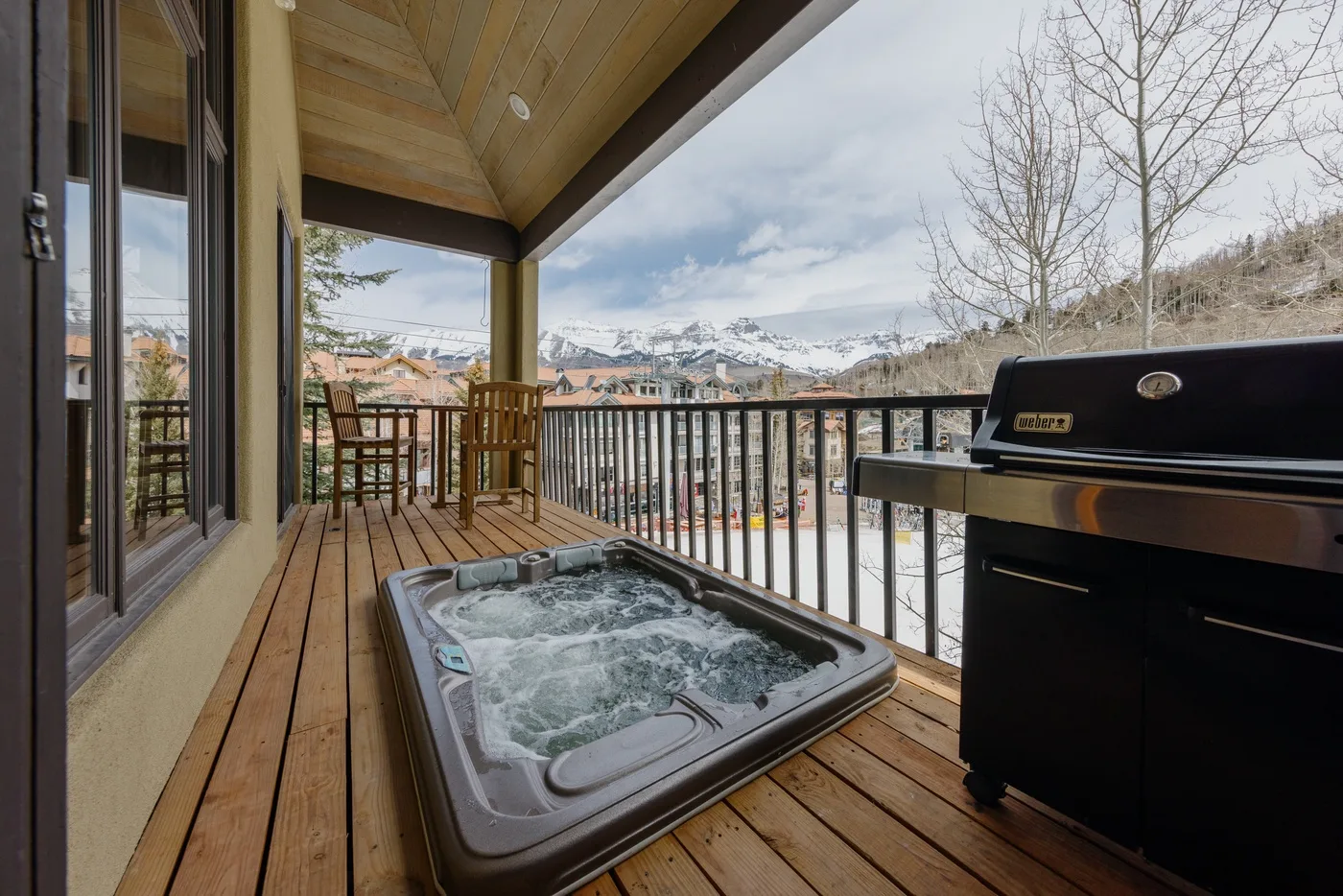 A covered wooden deck with a bubbling hot tub and mountain views.