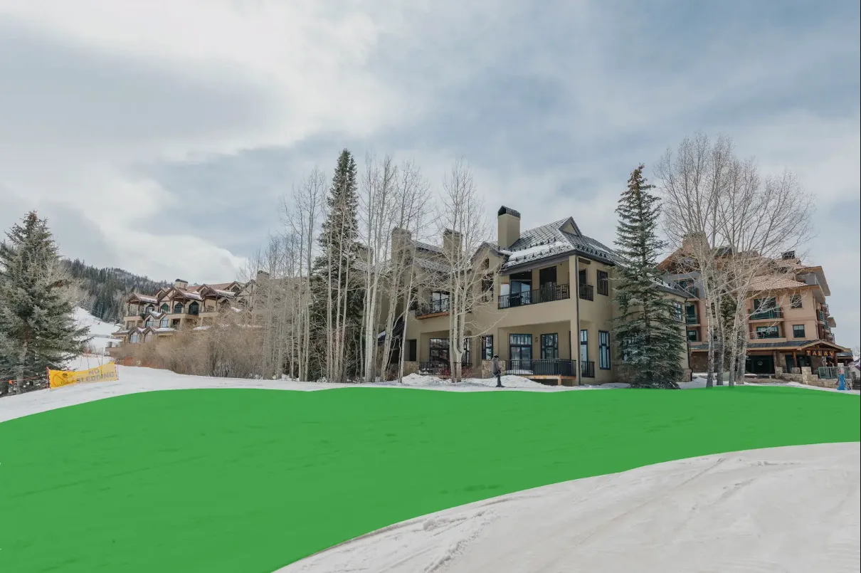 A large lodge-style building stands beside a snow-covered slope under a cloudy sky.