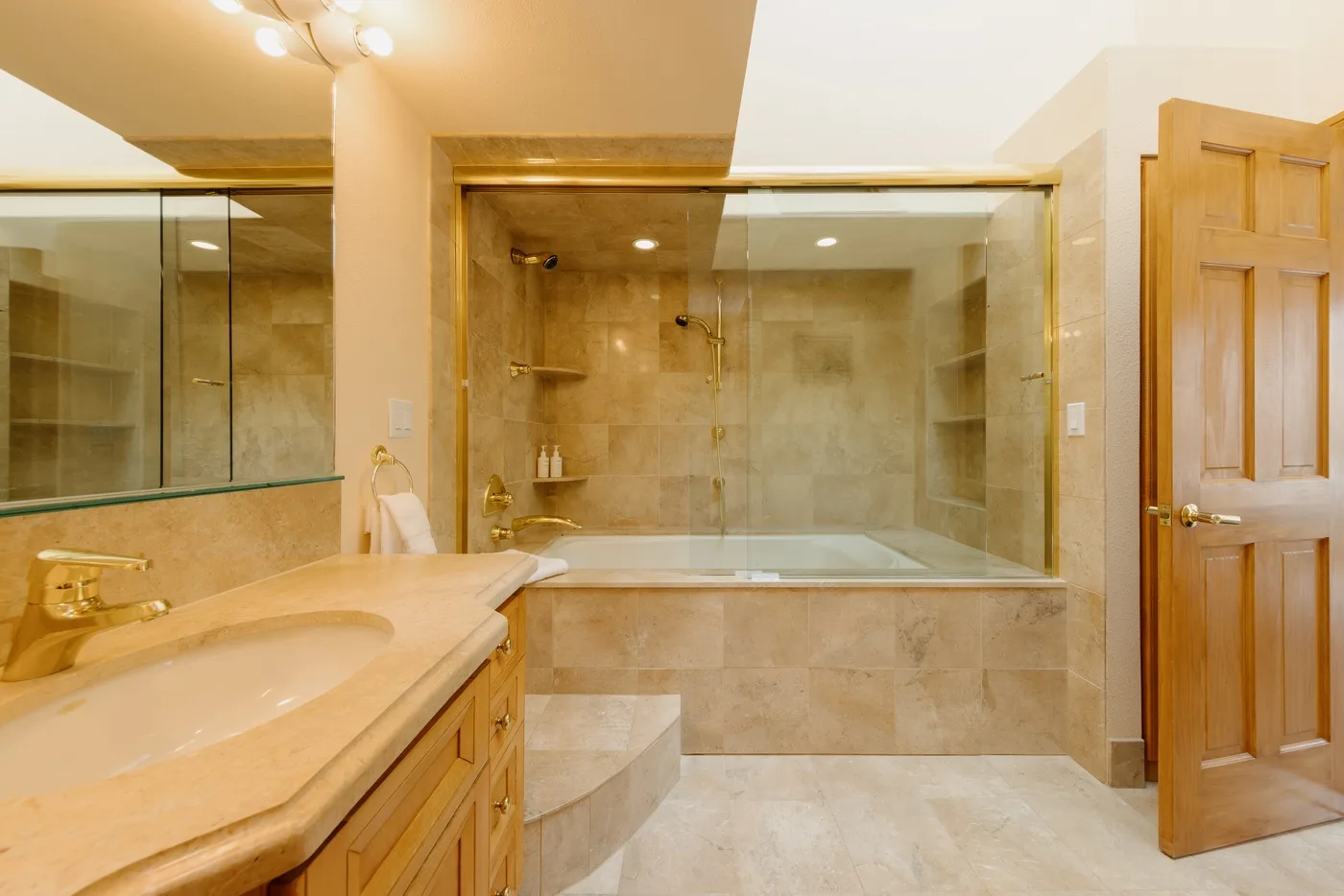 A bathroom with a long vanity and a glass-enclosed bathtub.