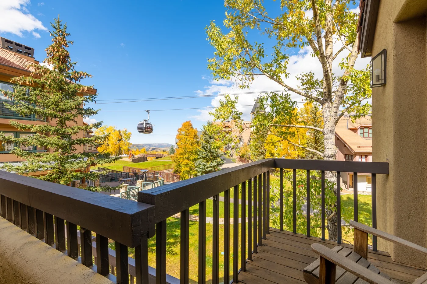 A wooden balcony overlooks colorful autumn trees and a distant gondola.