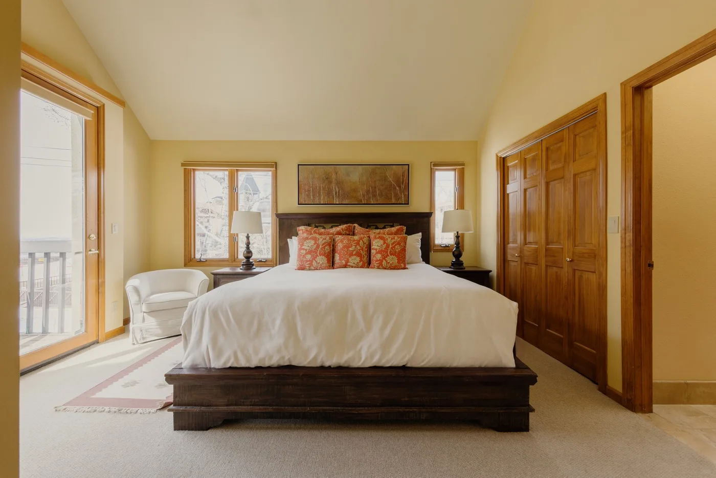 A bedroom with a large bed, patterned pillows, and windows on either side.