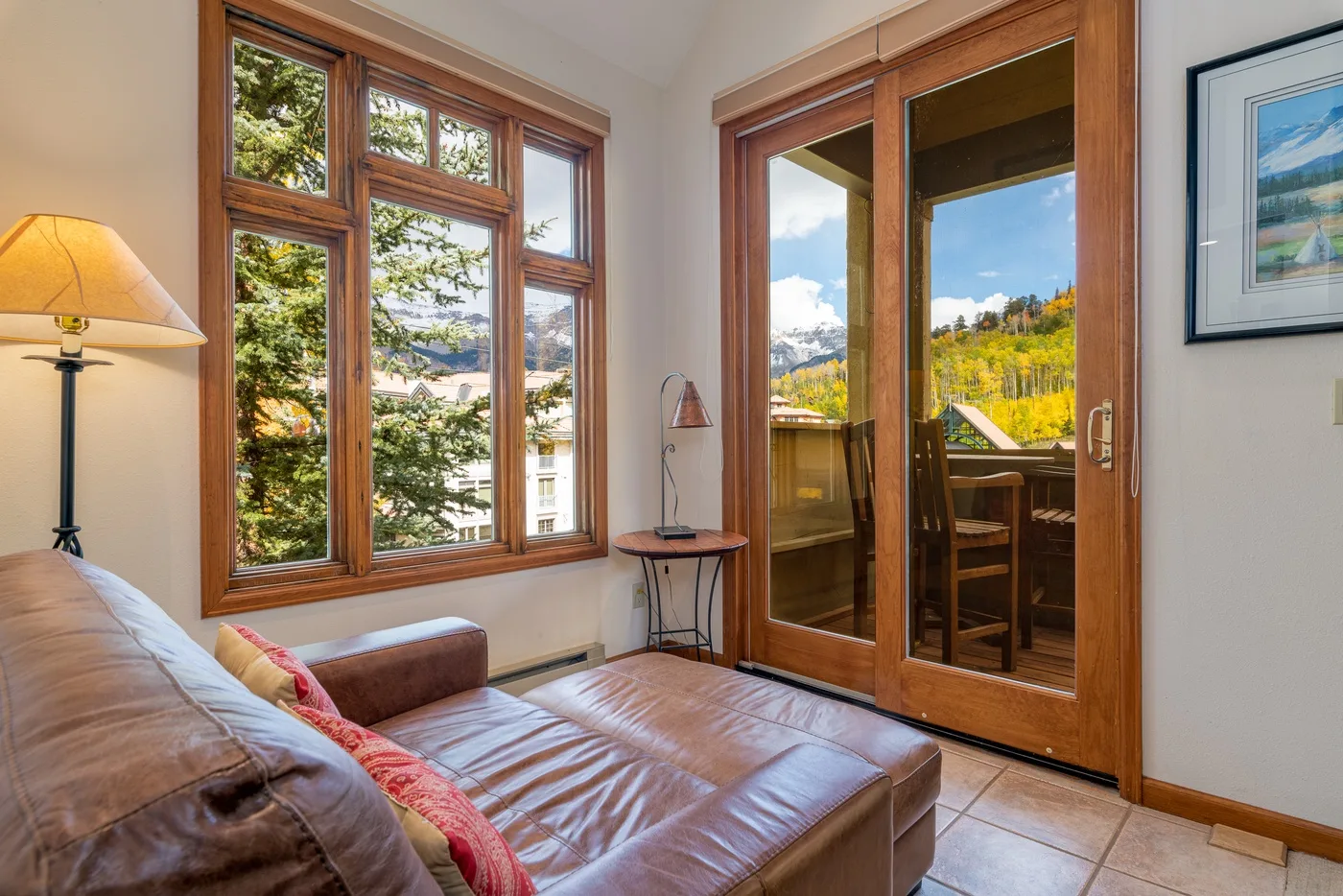 A sitting area with a leather sofa beside large windows and glass doors.